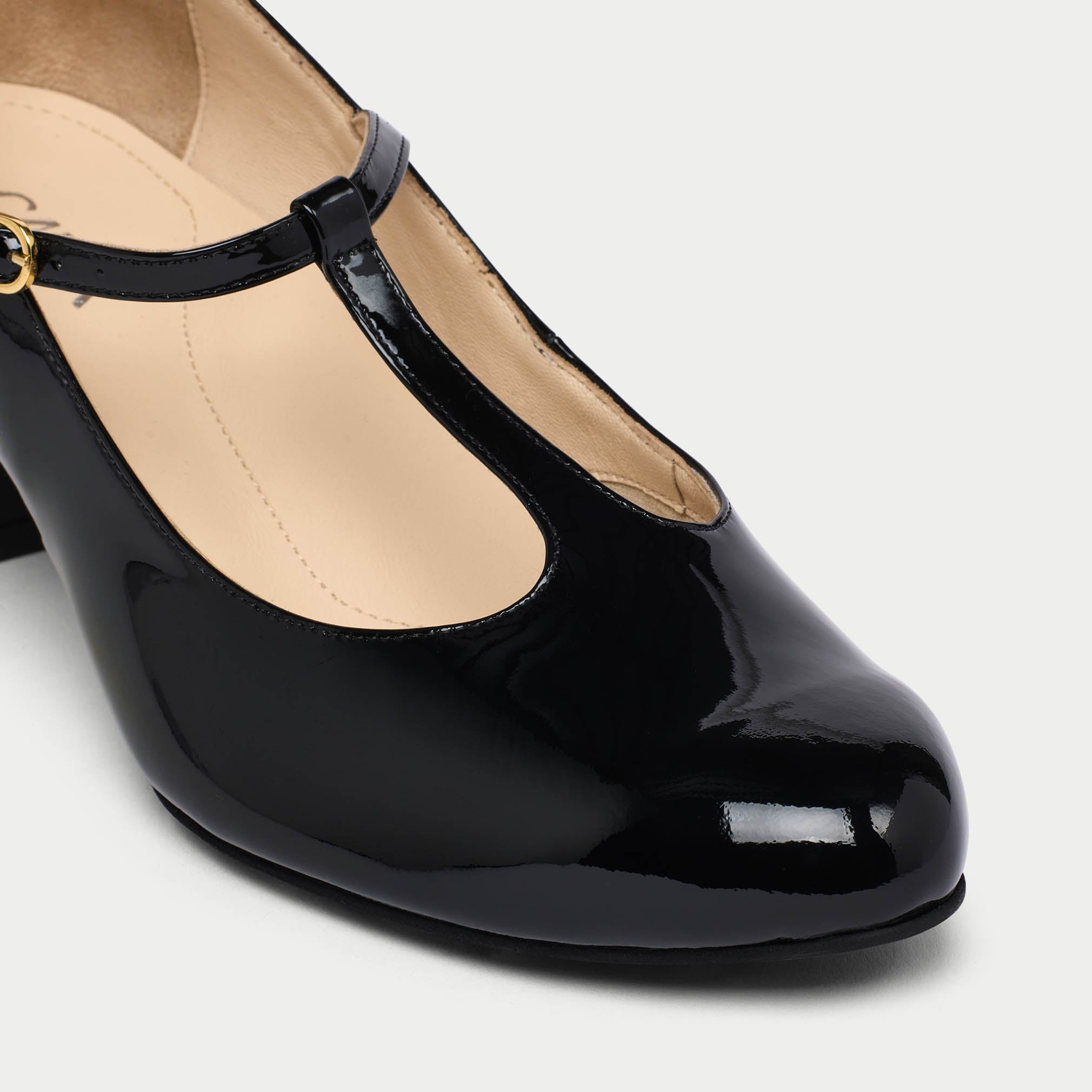 Black patent leather shoe with a gold buckle on a light gray background