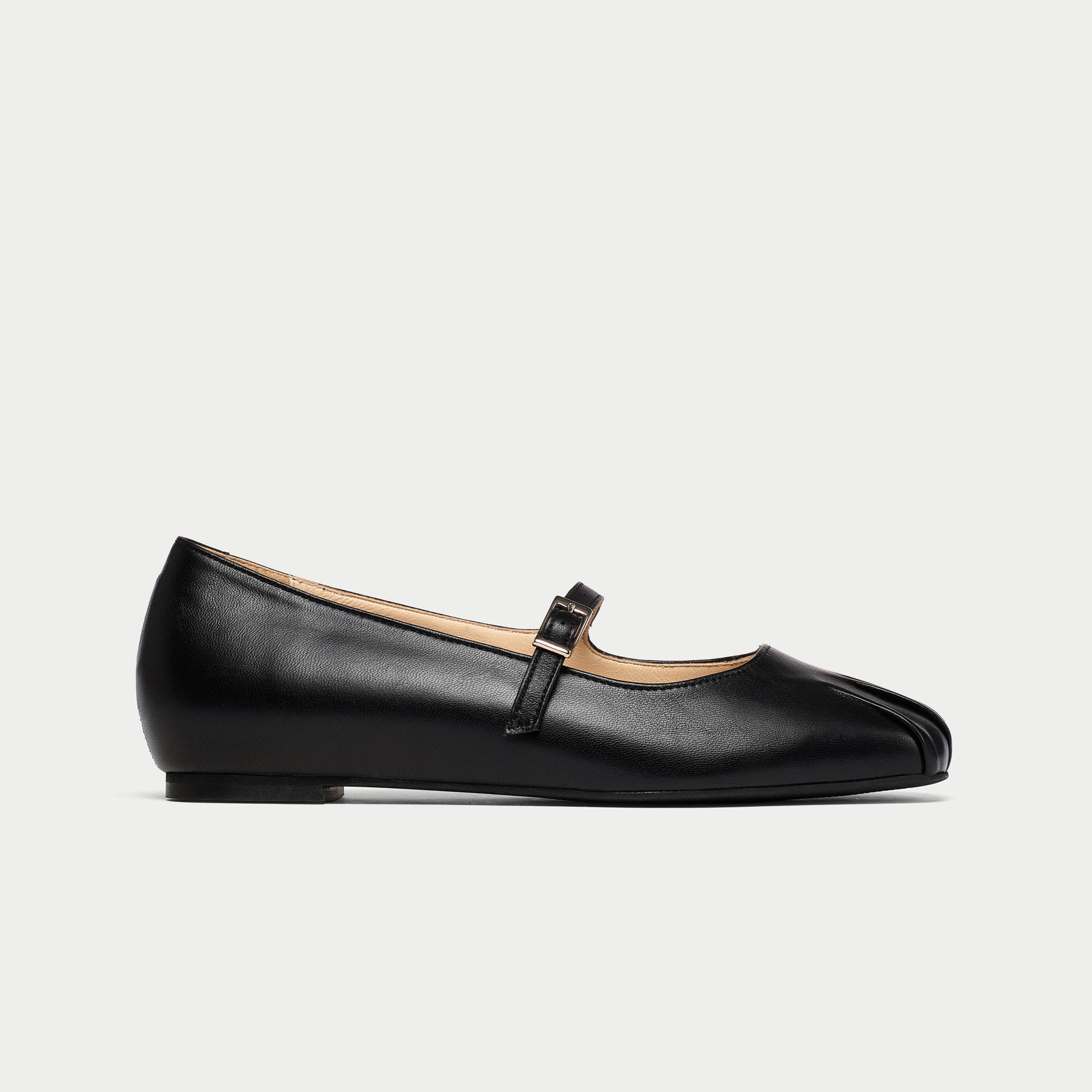 Black leather flat shoe with a strap on a light gray background