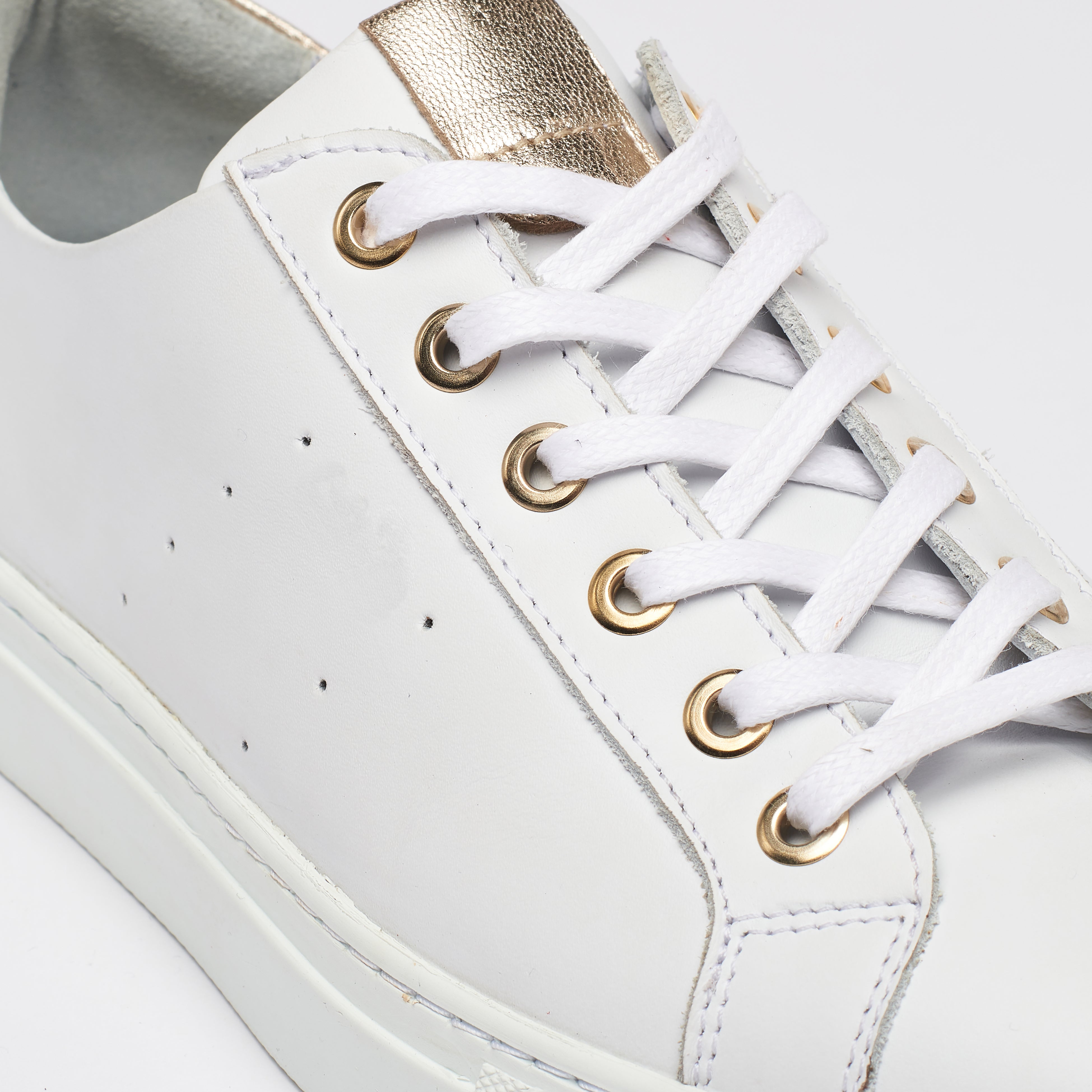 White sneaker with gold accents on a white background close up