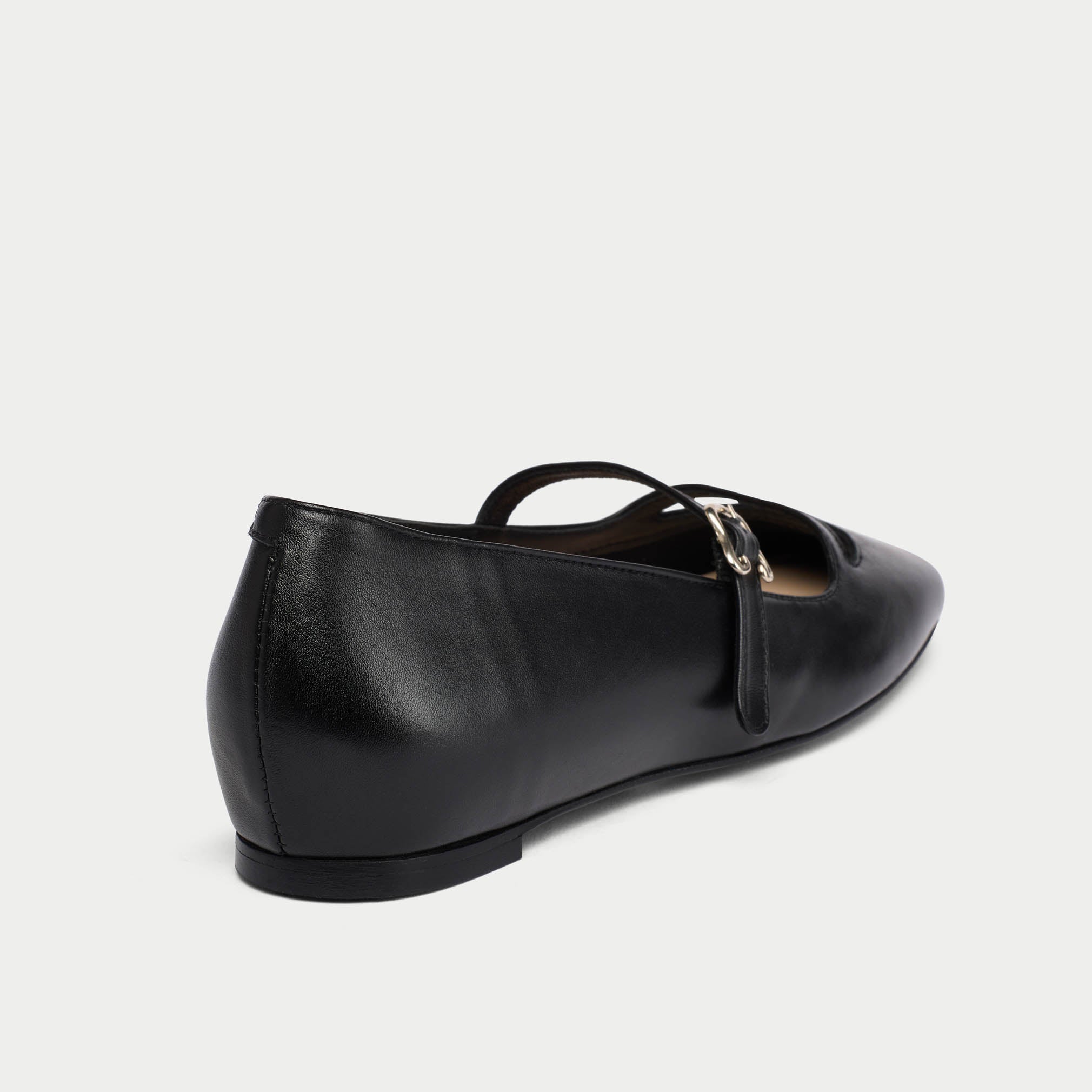 Black leather flat shoe with a gold buckle on a white background