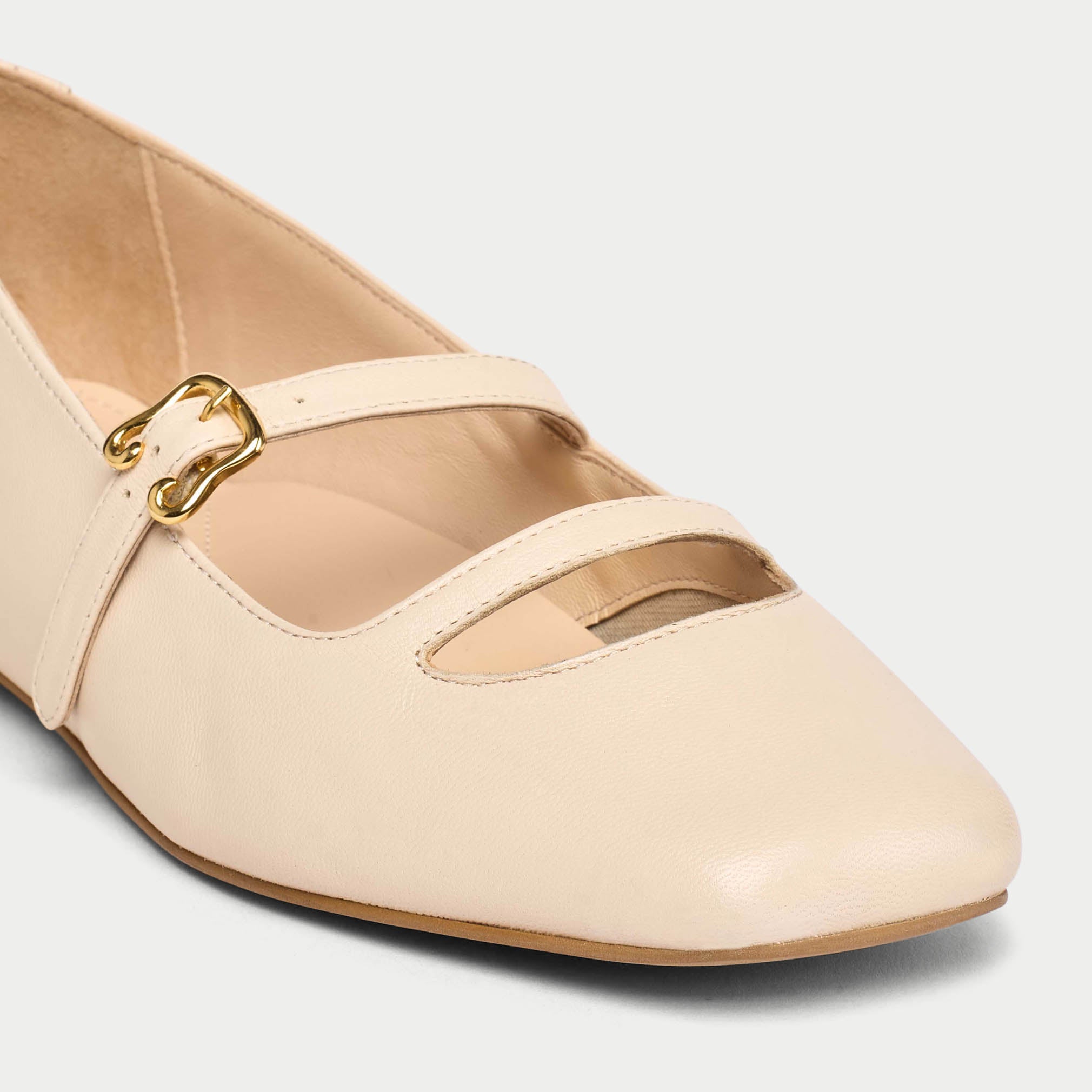 Beige flat shoe with a gold buckle on a light gray background