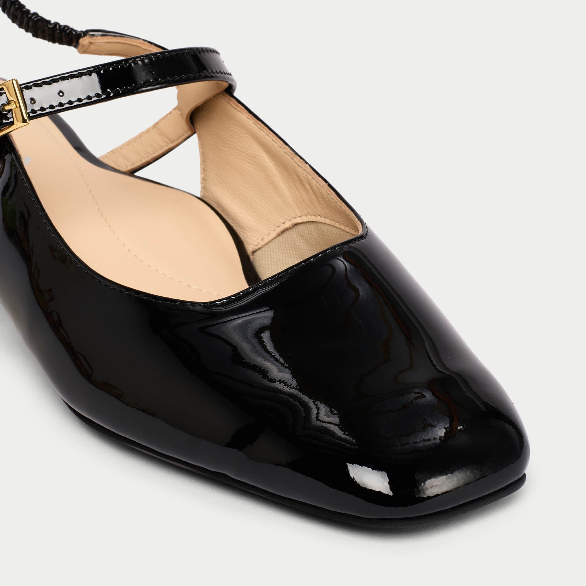 Black patent leathe shoe with a gold buckle on a light gray background
