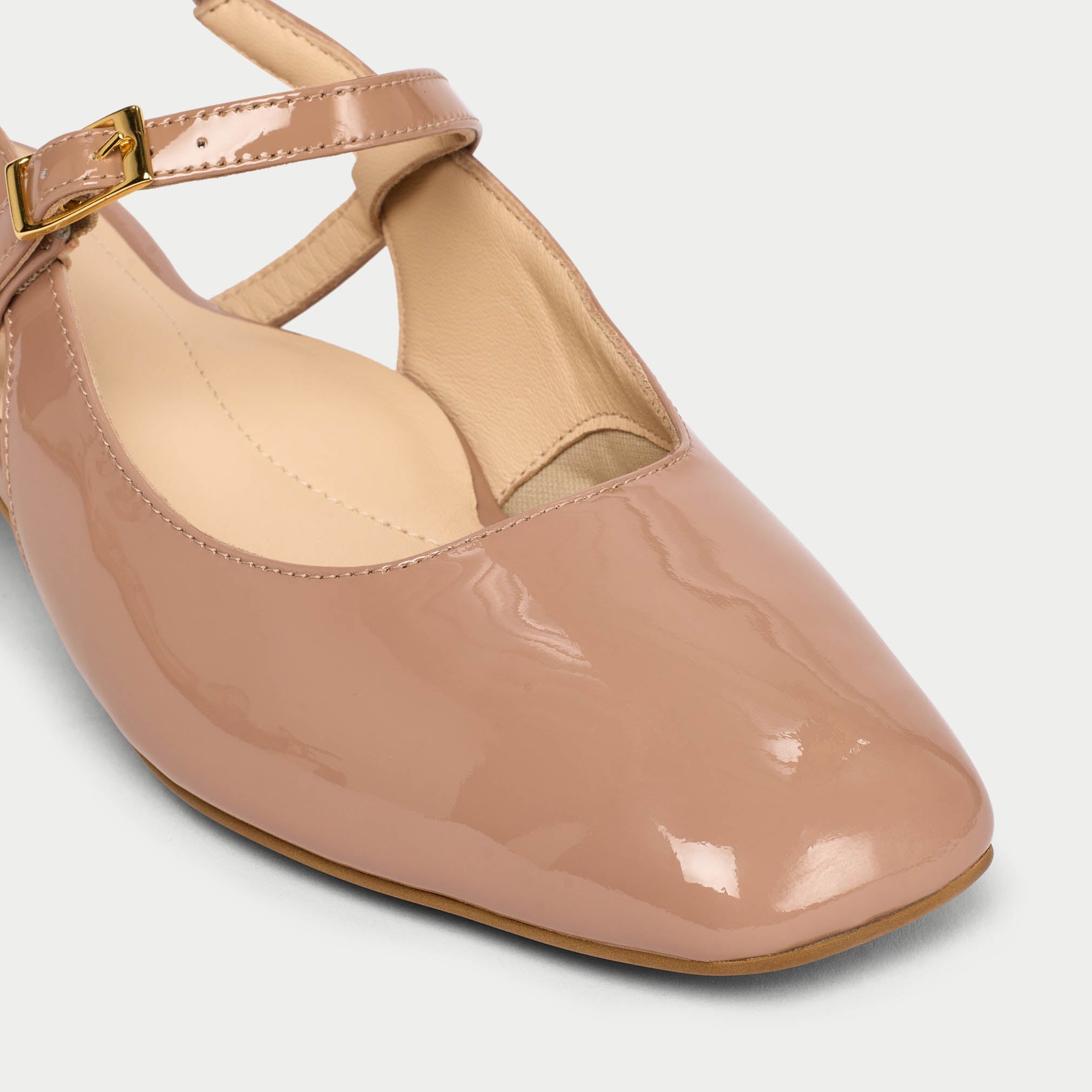Beige patent leather shoe with a gold buckle on a light gray background