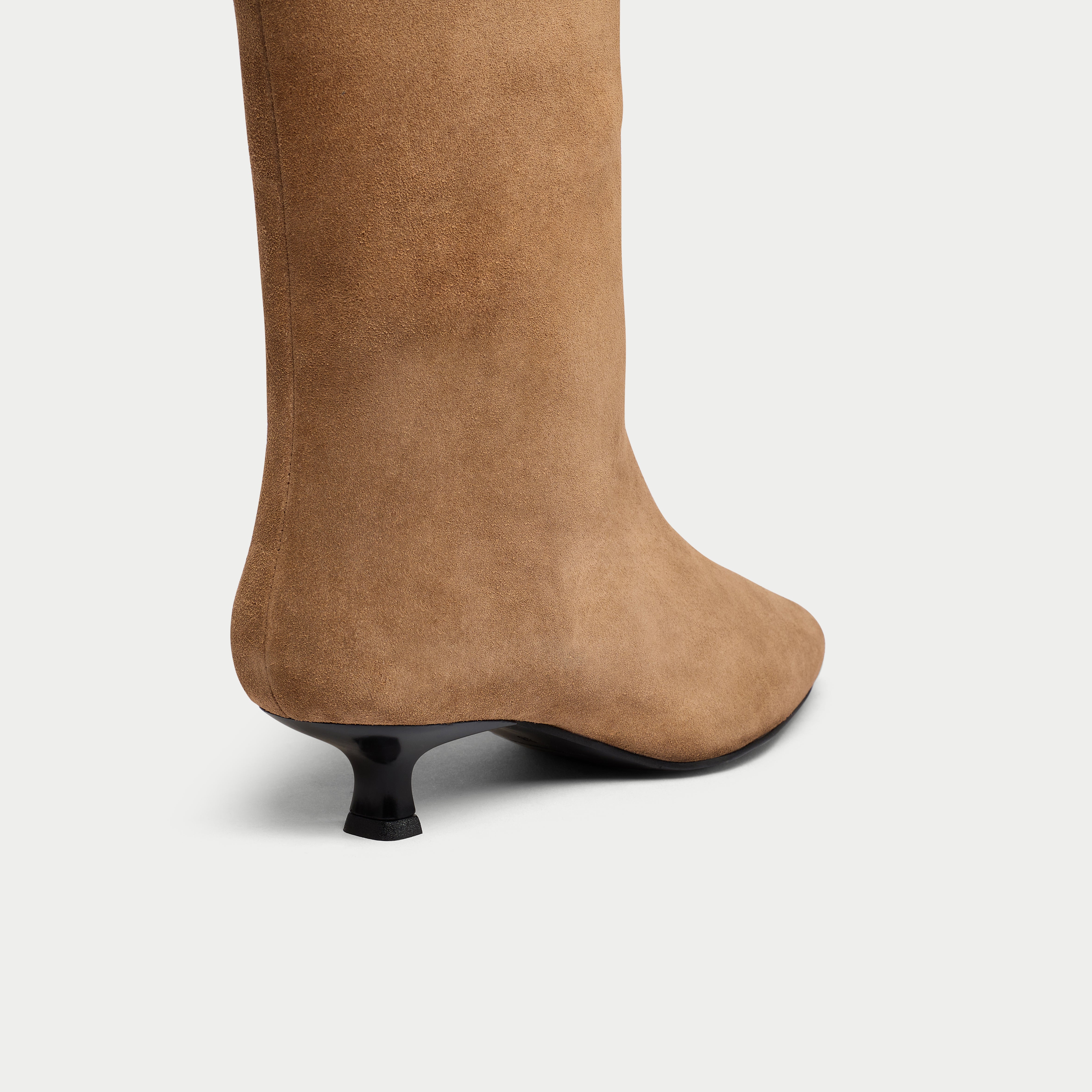 Tan knee-high boot with a black heel on a light gray background
