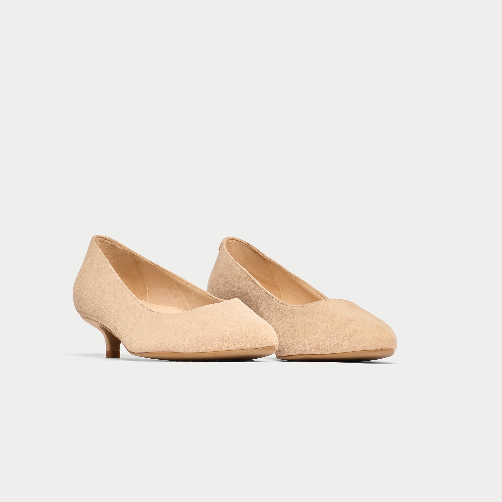 Pair of beige kitten heels on a light gray background