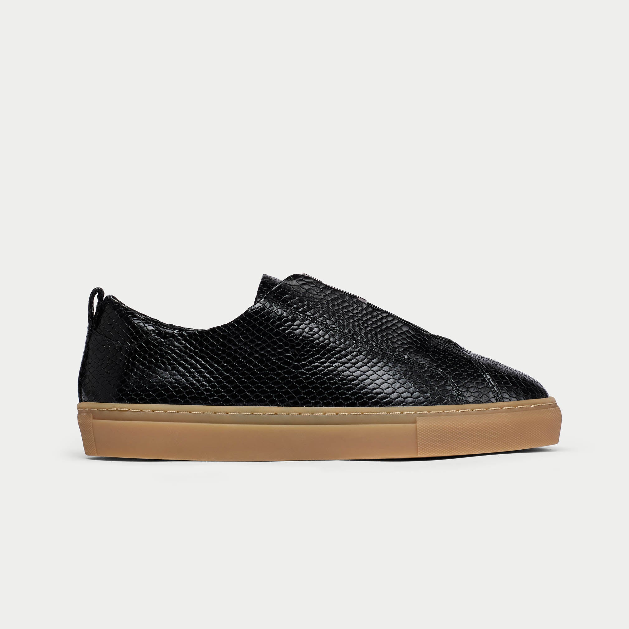 Black slip-on sneaker with brown sole on a light gray background