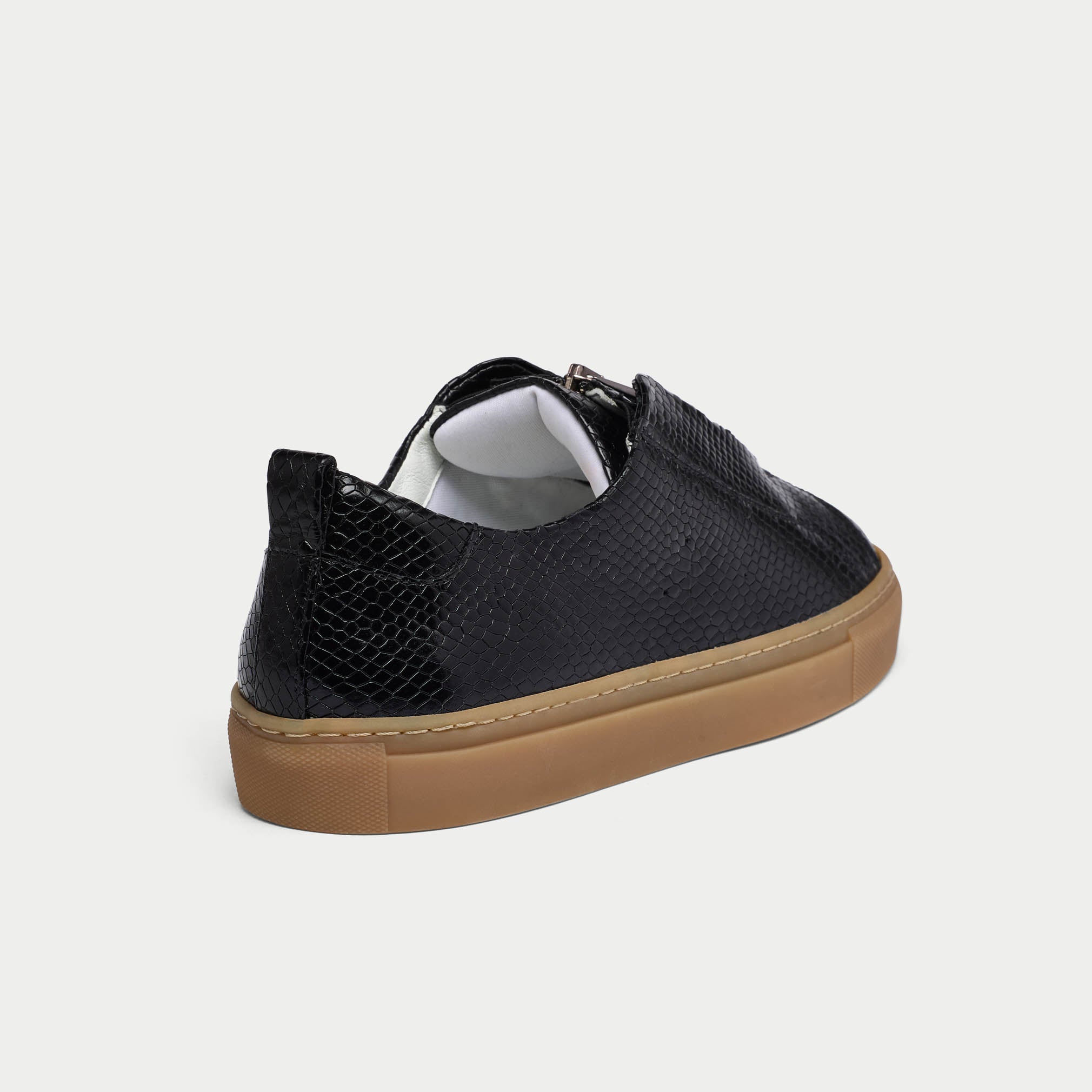 Black Estella sneaker with a brown sole on a light gray background heel close-up