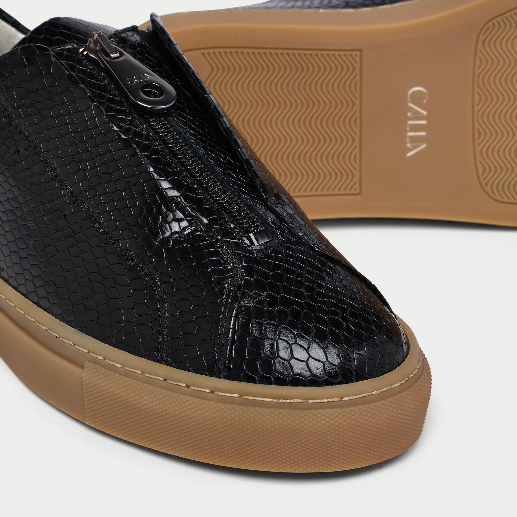 Black Estella snake-textured sneaker with brown sole on a white background tip close-up