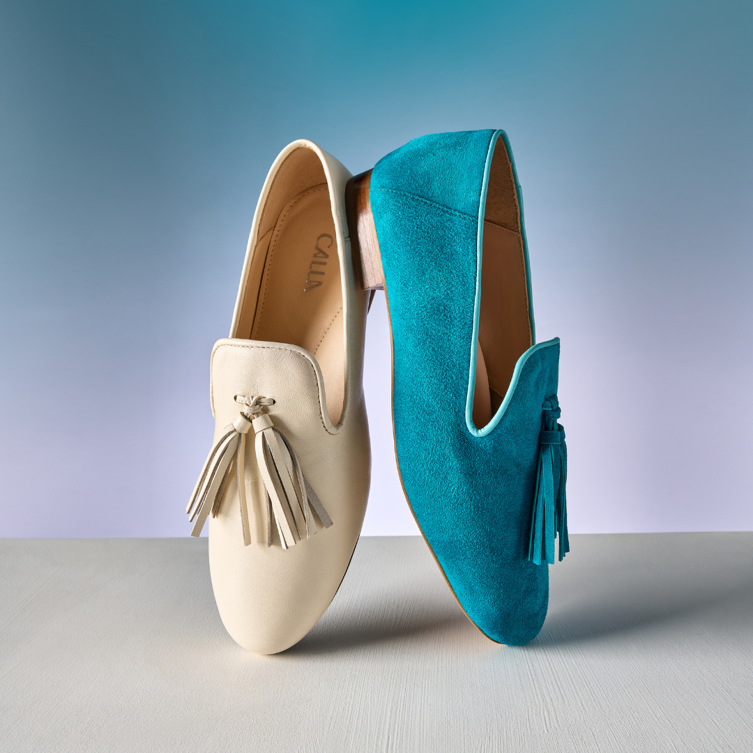 Pair of cream and turquoise loafers with tassels on a gradient background