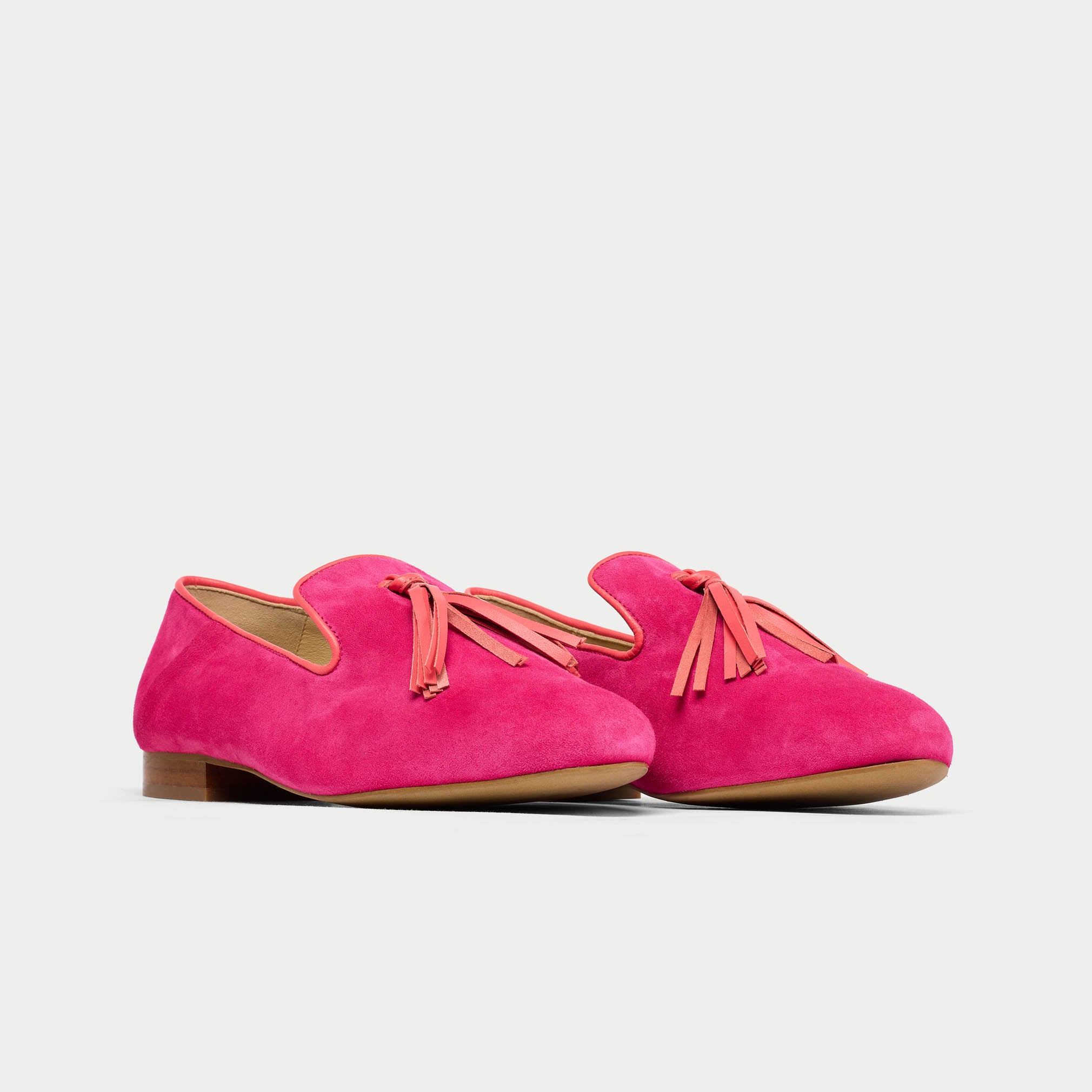 Pair of bright pink suede shoes with orange laces on a light gray background