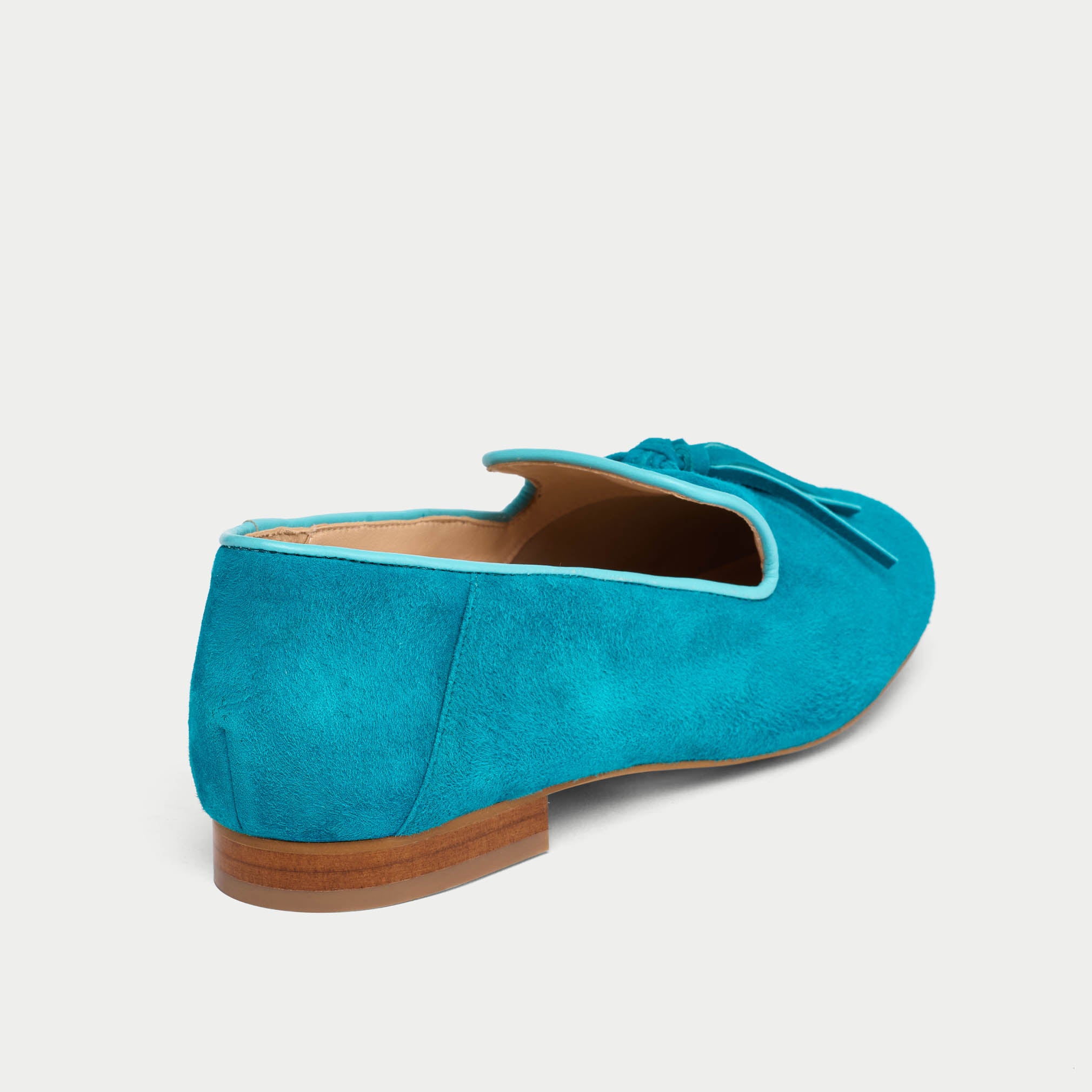 Blue suede loafer with a brown sole on a light gray background