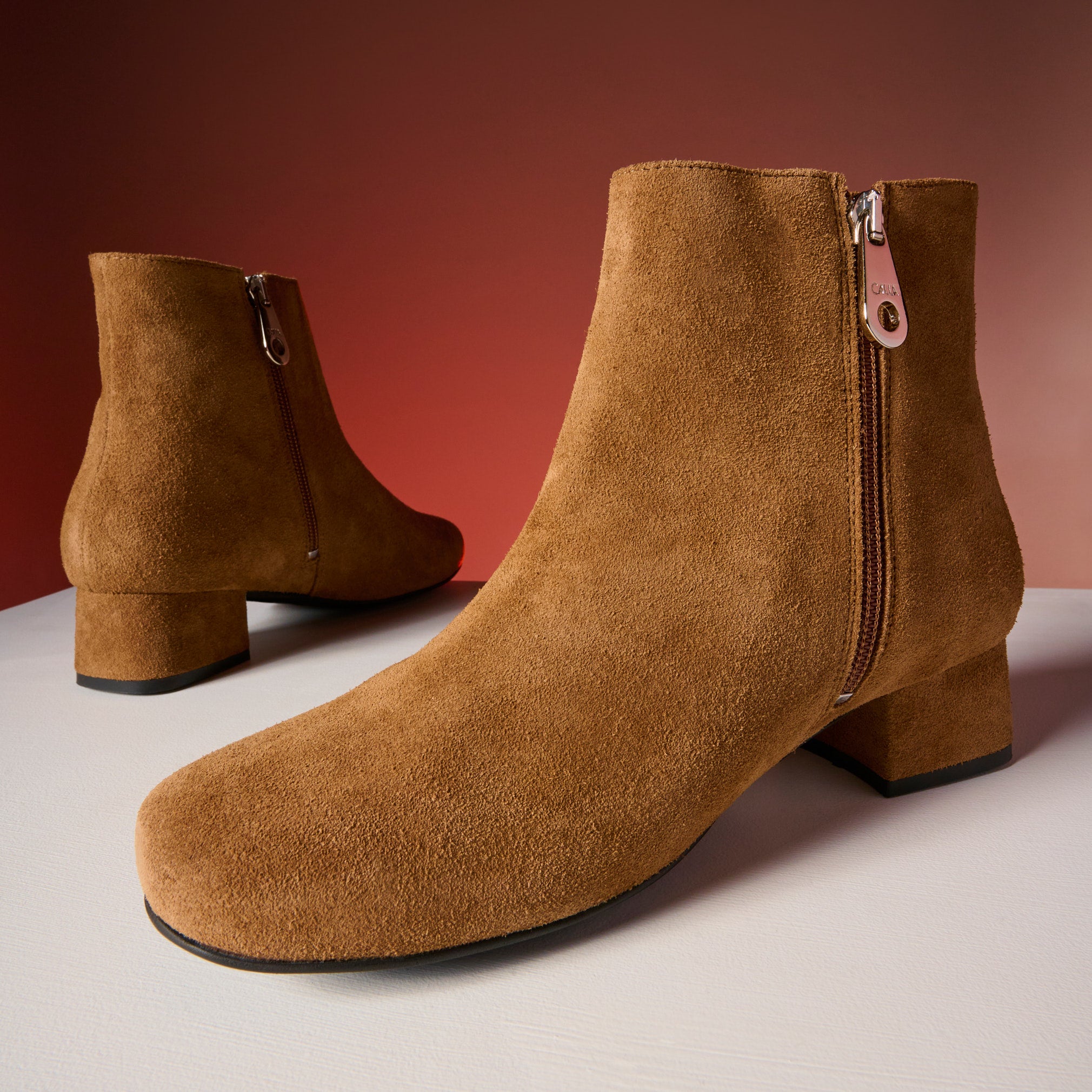 Pair of brown suede ankle boots with zippers on a gradient background