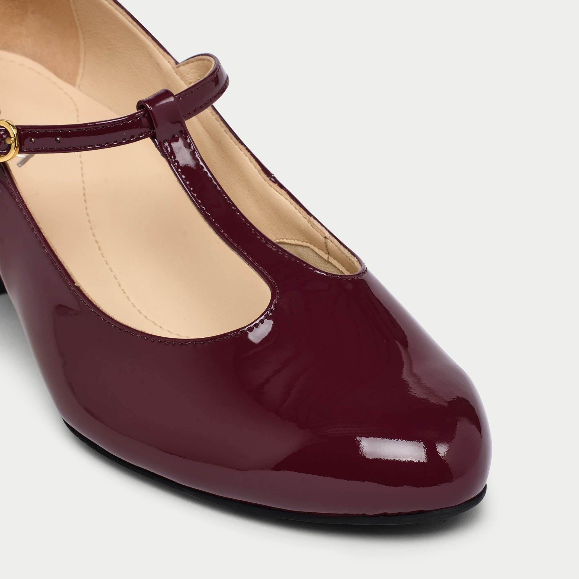 Maroon high-heeled shoe with a strap on a light gray background