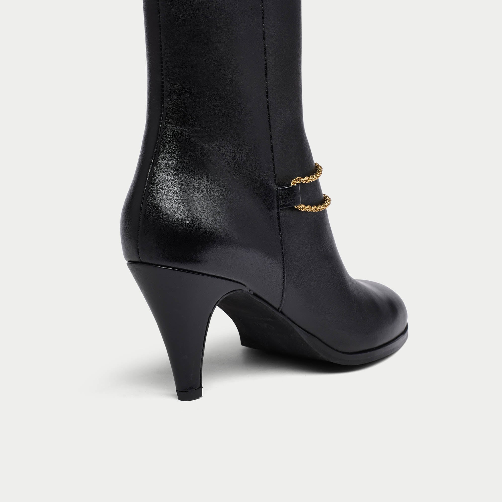 Black Maya boot with gold chain detail on a white background heel close-up