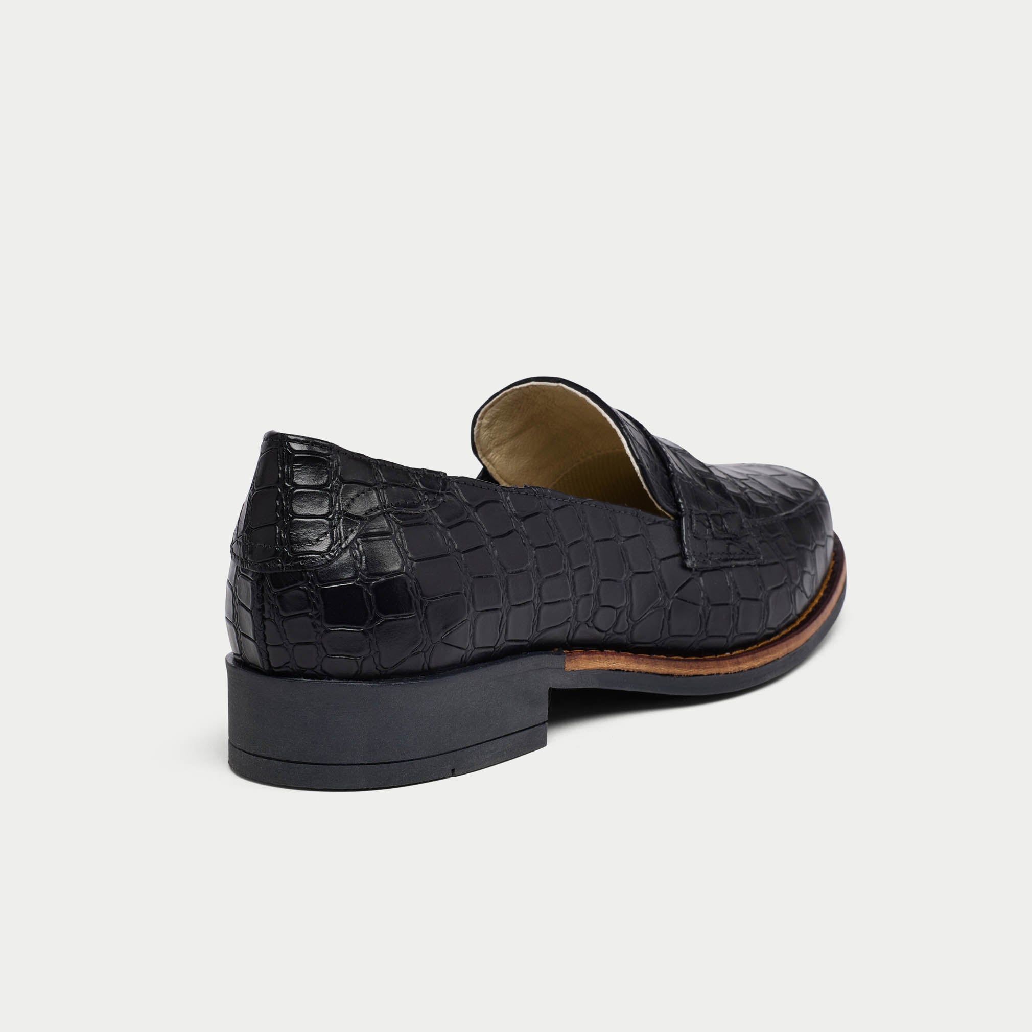 Black Nadia crocodile-patterned loafer shoe on a light gray background heel close-up
