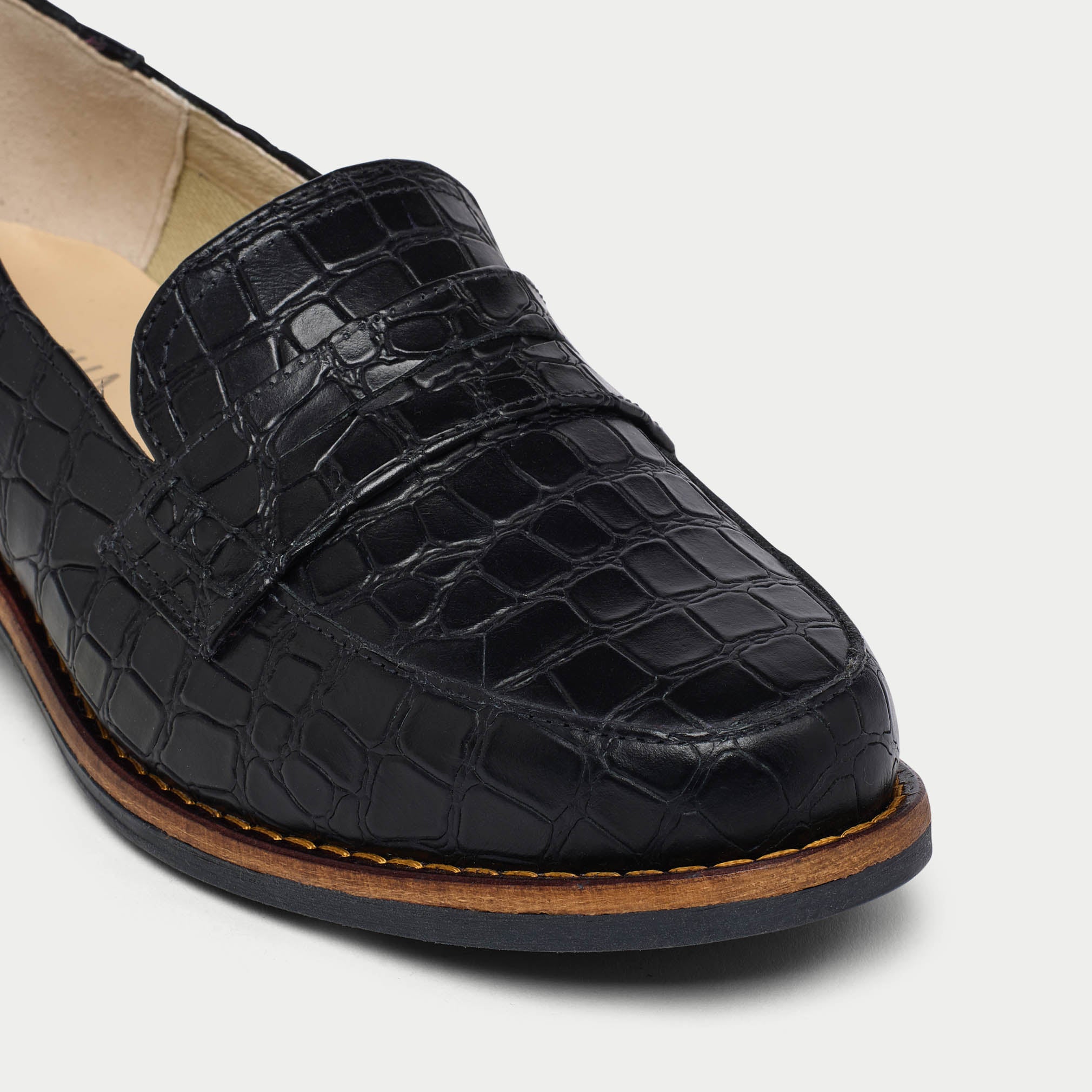Black Nadia crocodile-patterned loafer shoe on a light gray background tip close-up