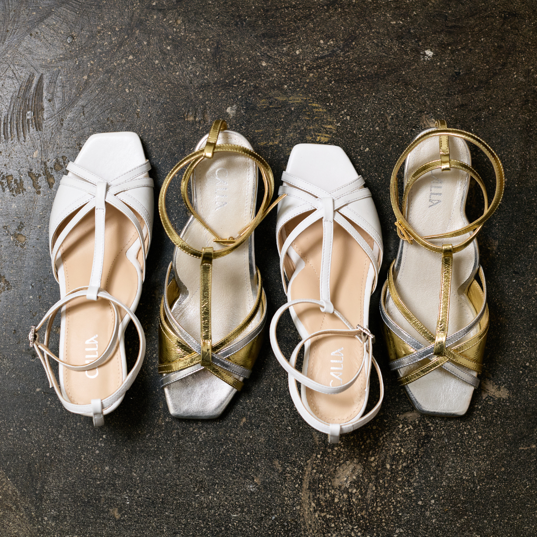 Pair of white and gold kitten-heeled sandals on a textured dark surface