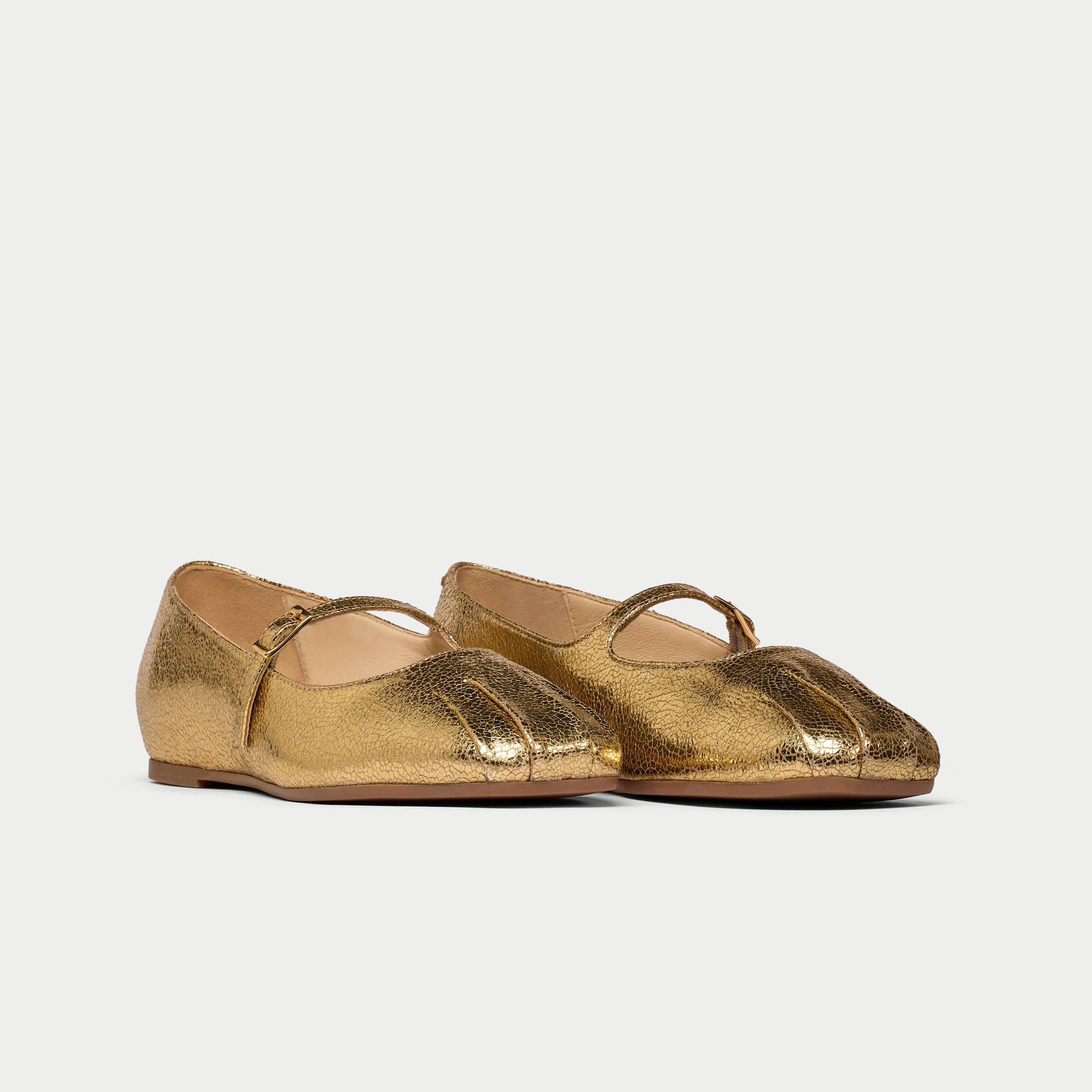 Pair of gold metallic flats on a light gray background