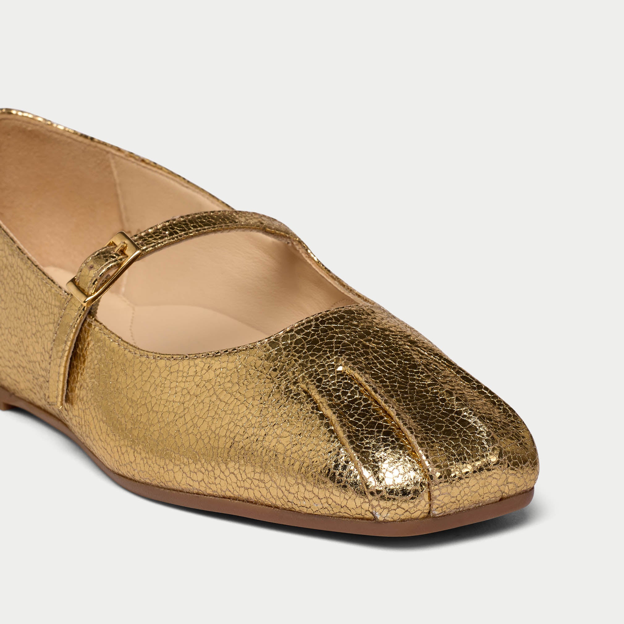 Gold metallic flat shoe with a strap on a light gray background