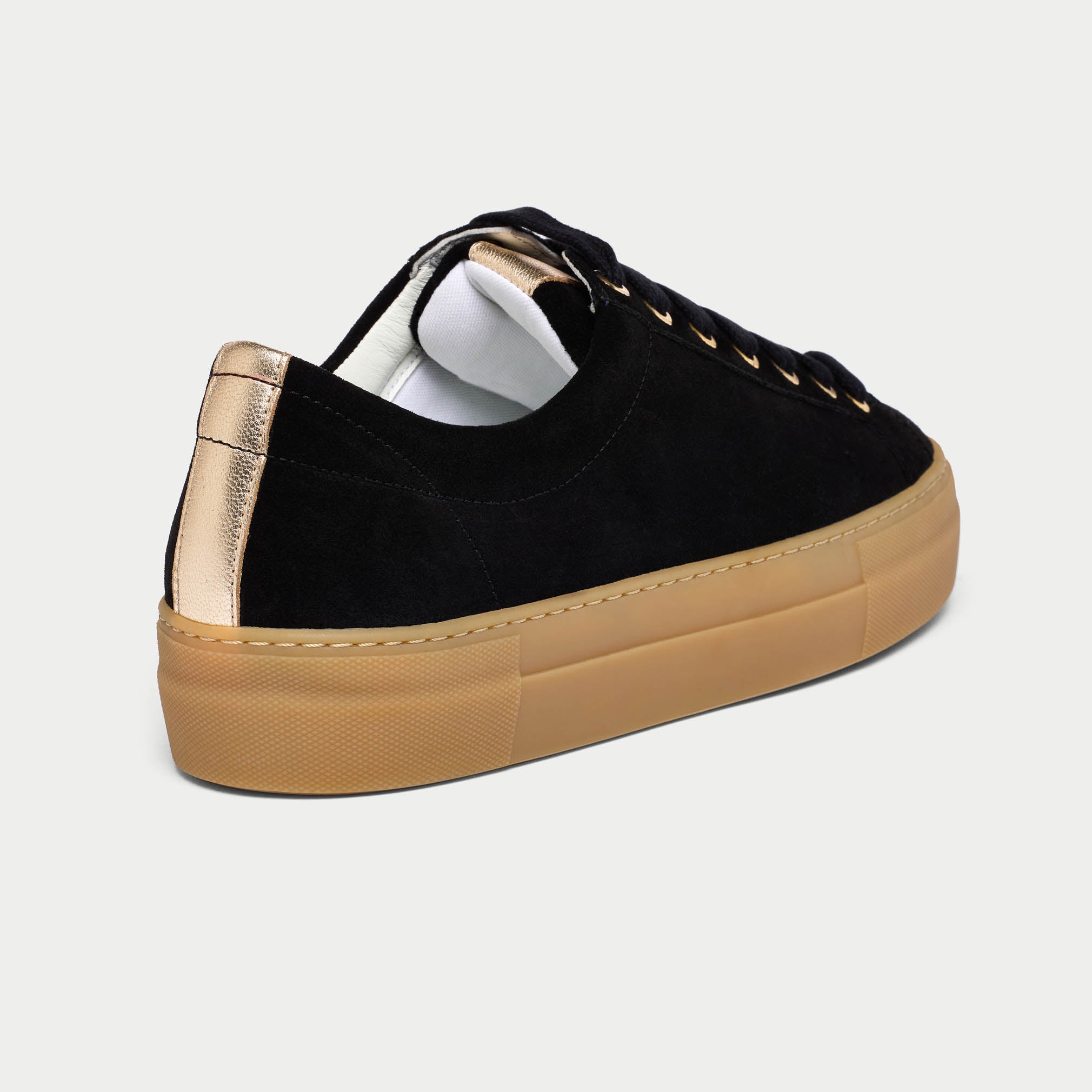 Black Saturn sneakers with tan soles and gold accents on a light gray background back close-up