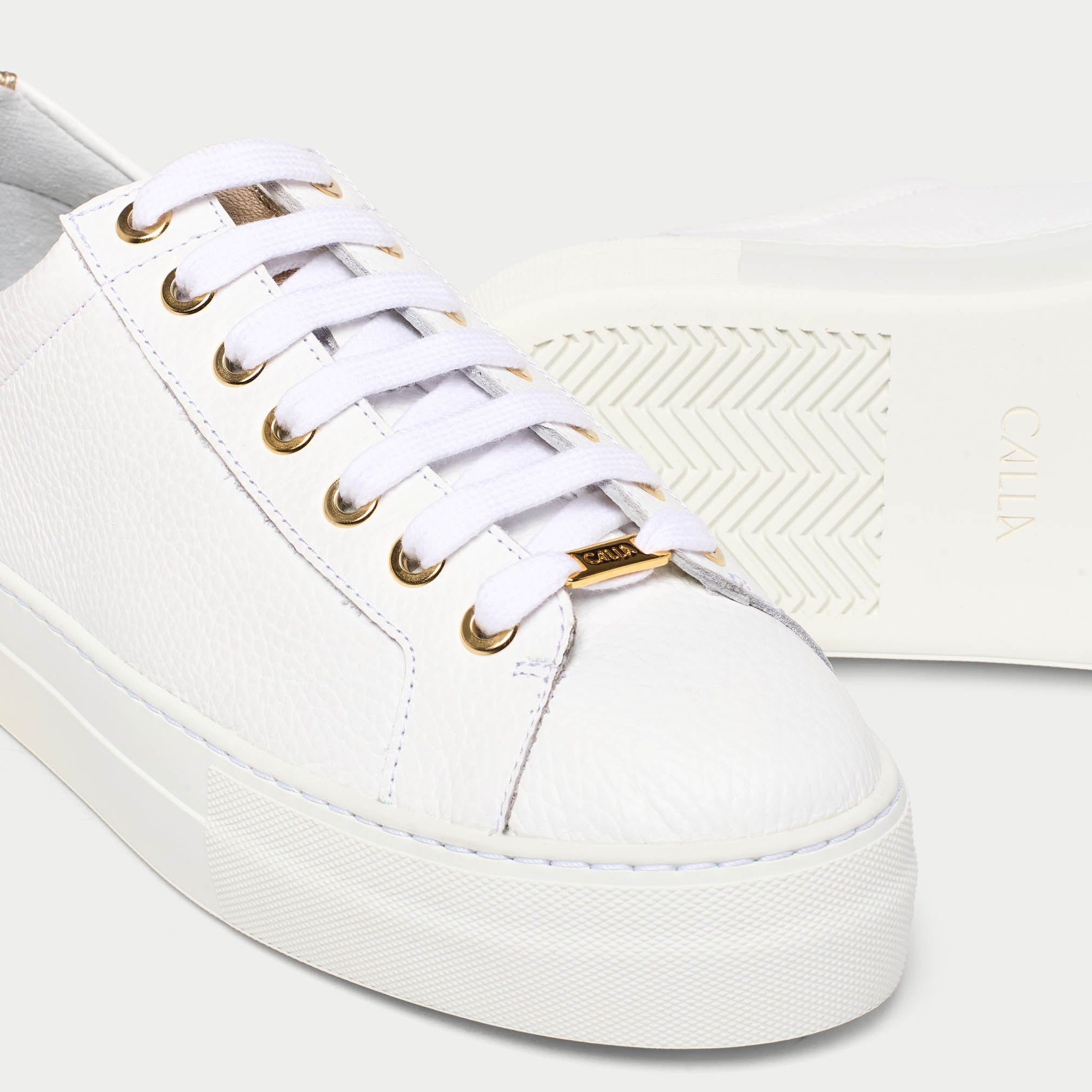 White saturn sneaker with gold accents on a light gray background tip close up
