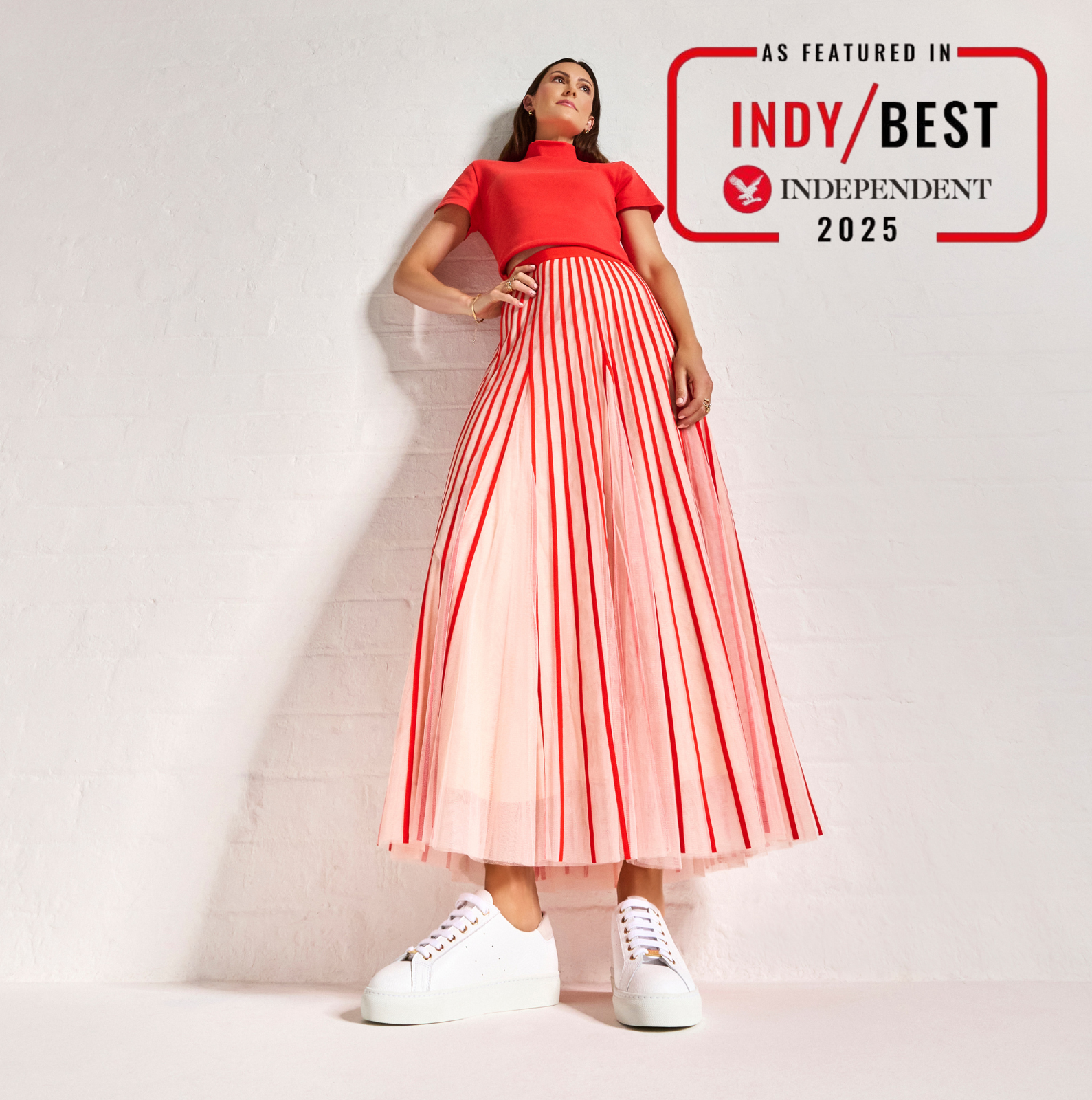 Woman wearing a red top and pink pleated skirt with 'Indy Best Independent 2025' badge on a light background