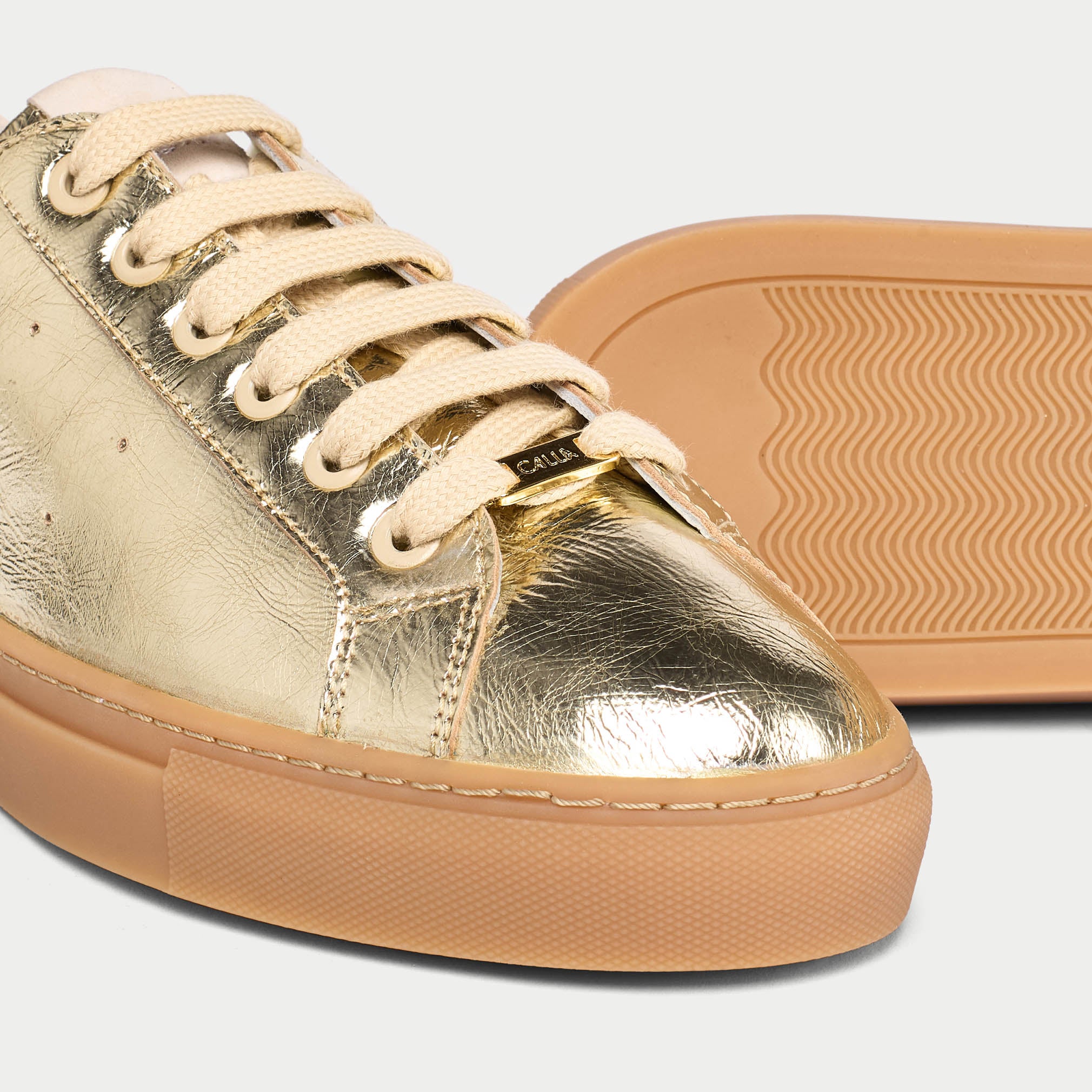 Gold sneaker with beige laces and sole on a light gray background