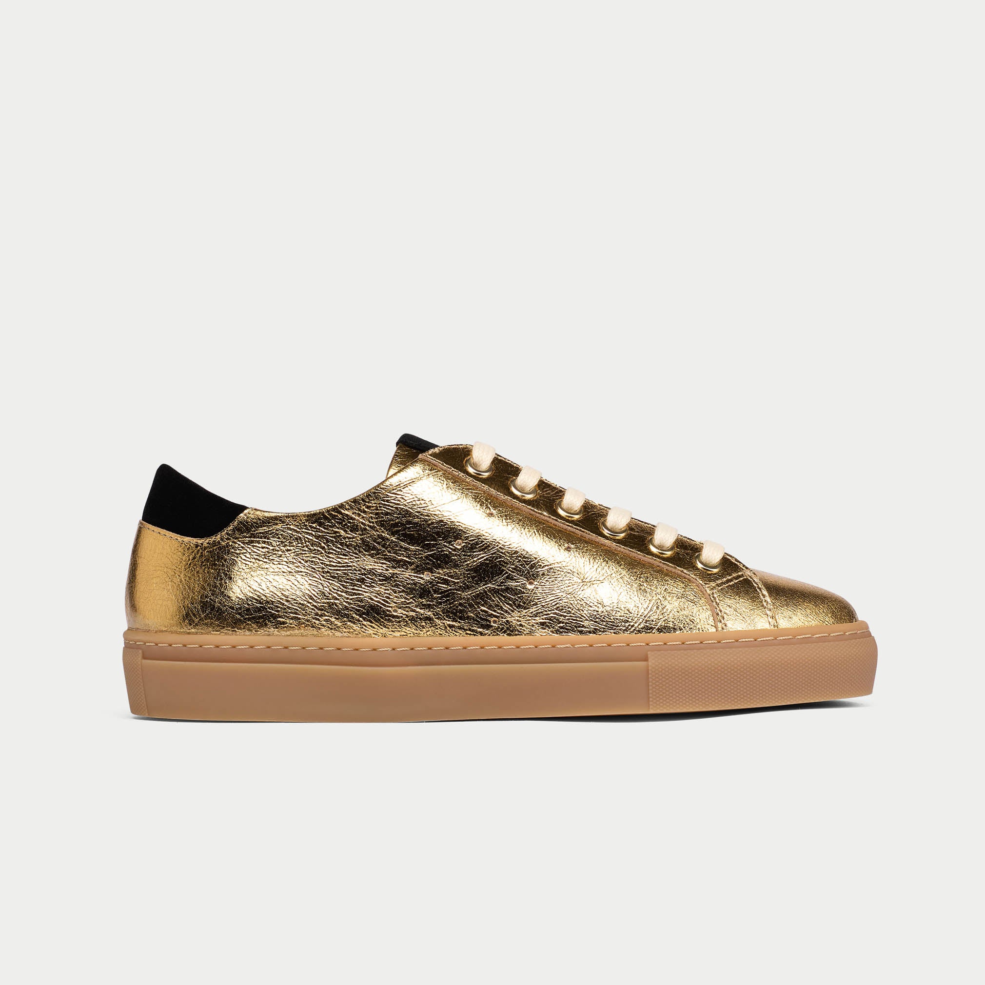 Gold sneaker with a brown sole on a light gray background
