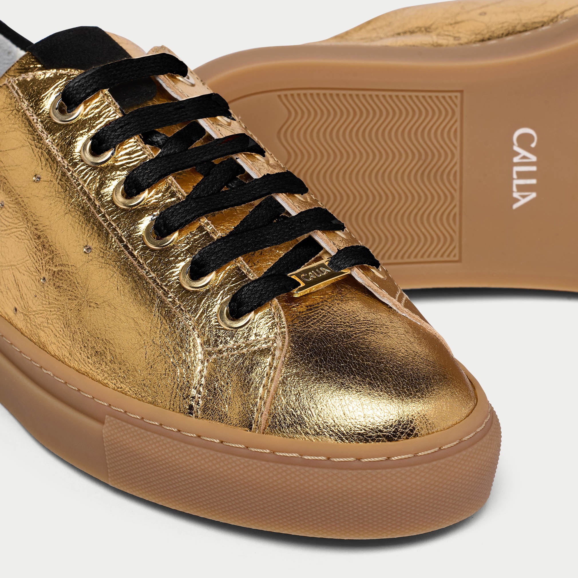 Gold sneaker with black laces and brown sole on a white background