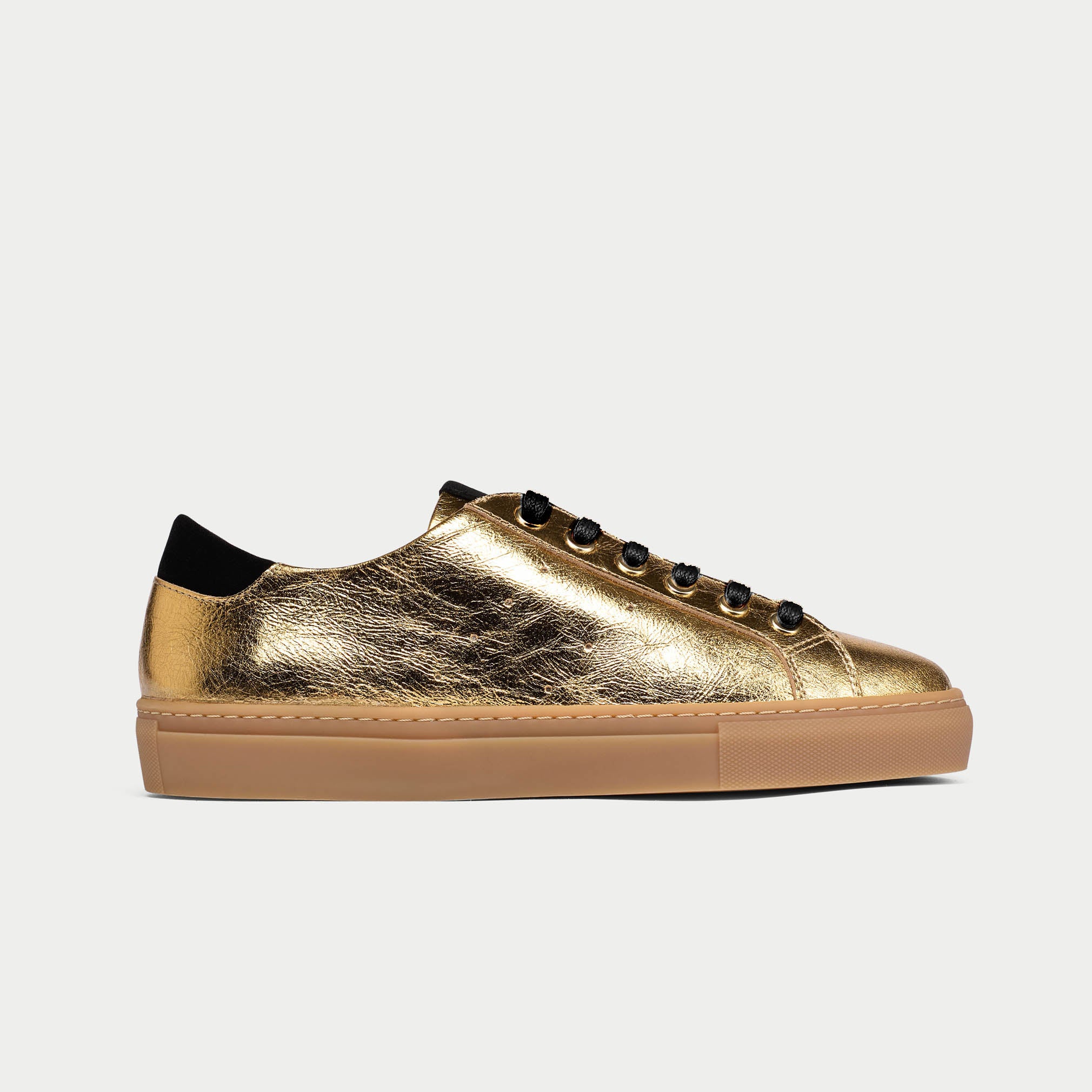 Gold sneaker with black accents on a light gray background