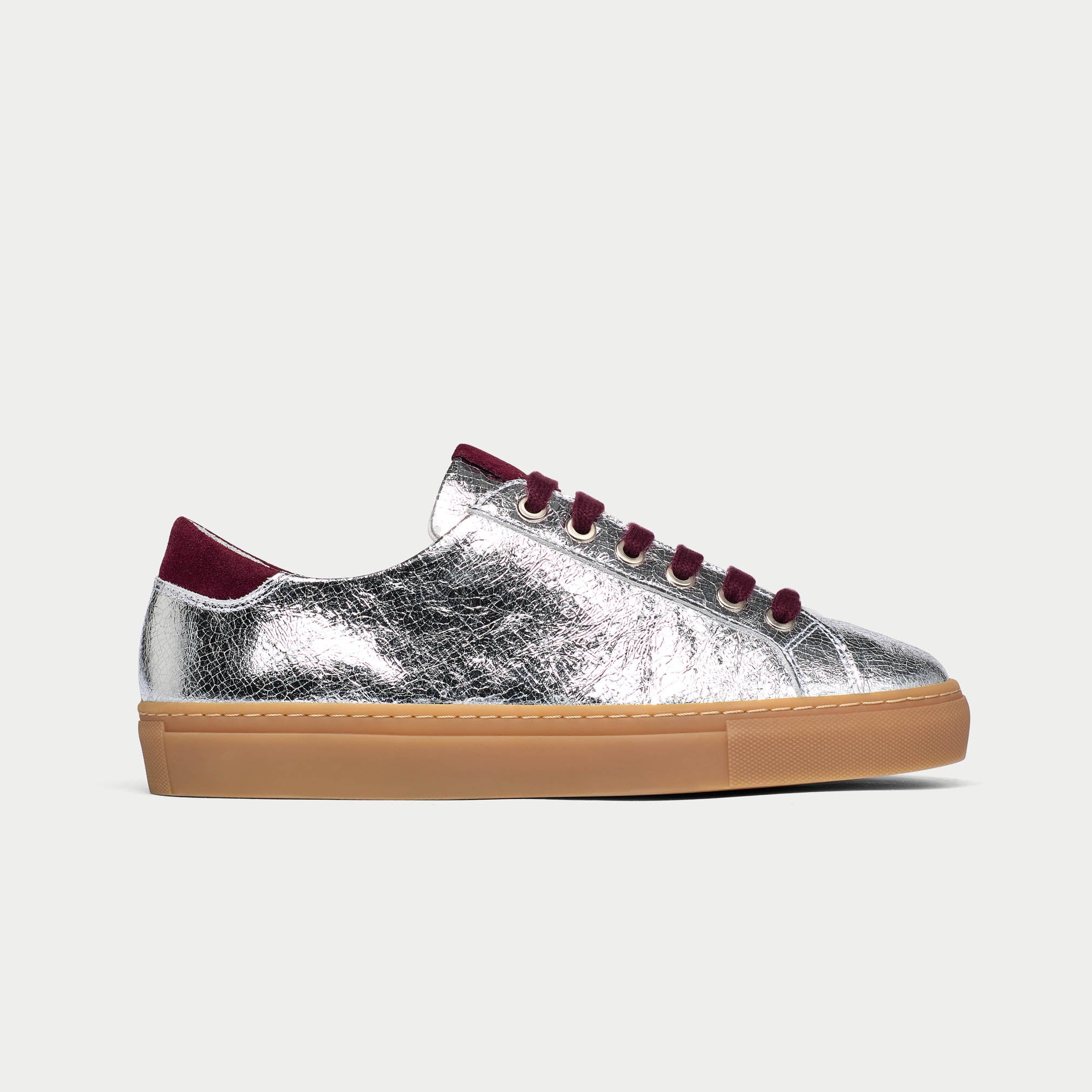 Silver sneaker with burgundy laces and sole on a light gray background