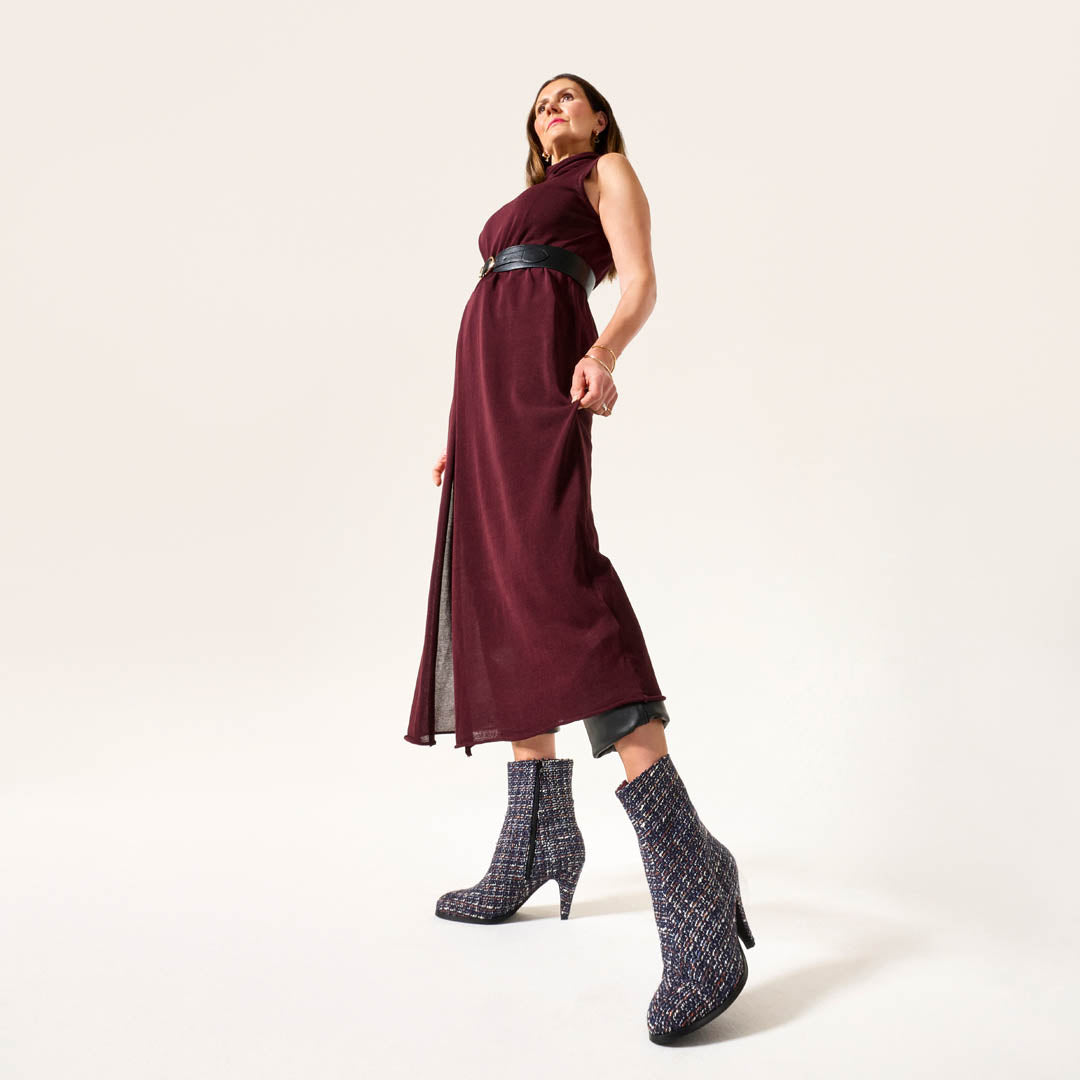 Woman wearing a burgundy dress with a black belt and patterned Maya boots on a white background