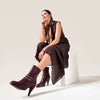 Woman wearing Cherry Maya boots for bunions with gold buckles sitting on a white stool against a light background