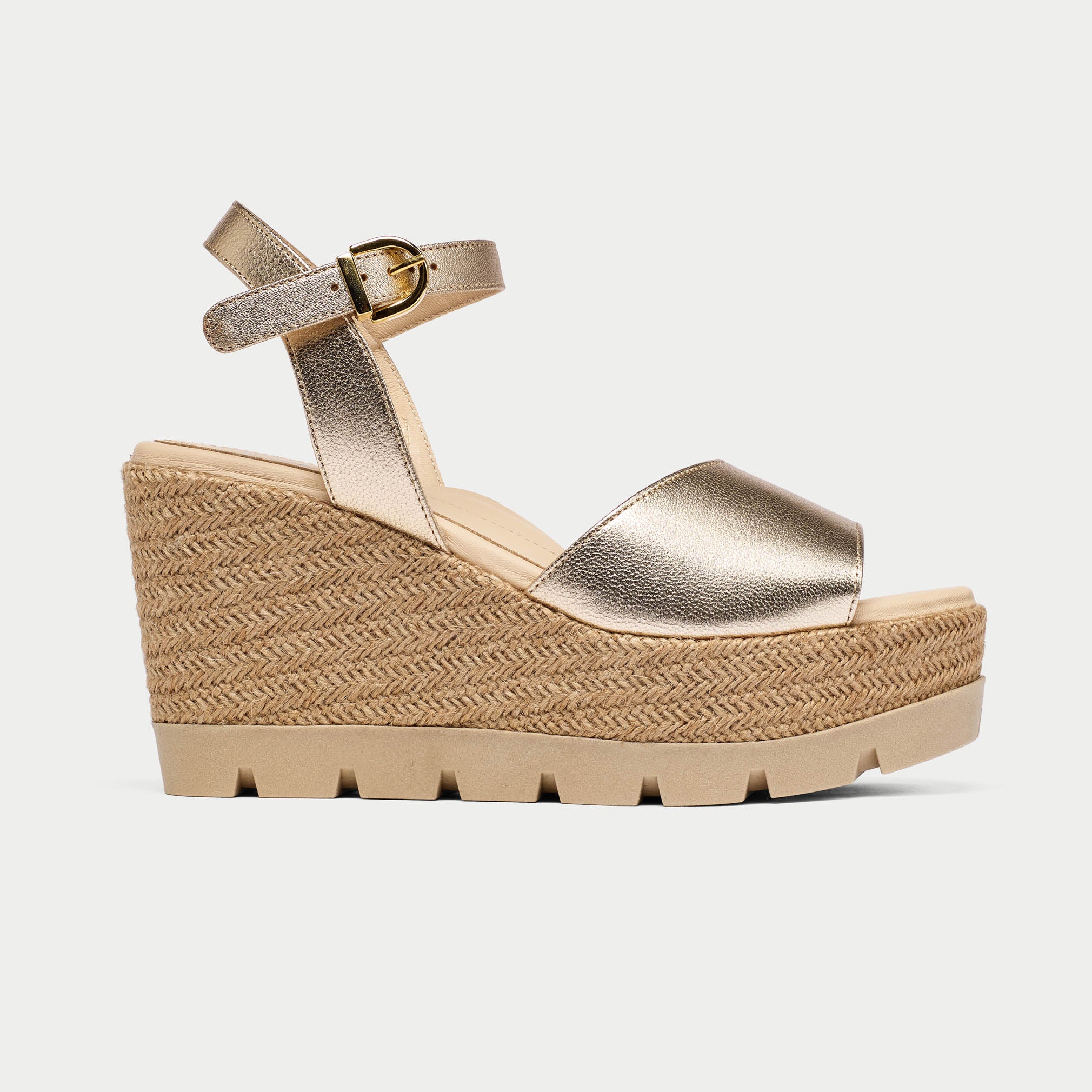 Gold wedge sandal with espadrille sole on a light gray background