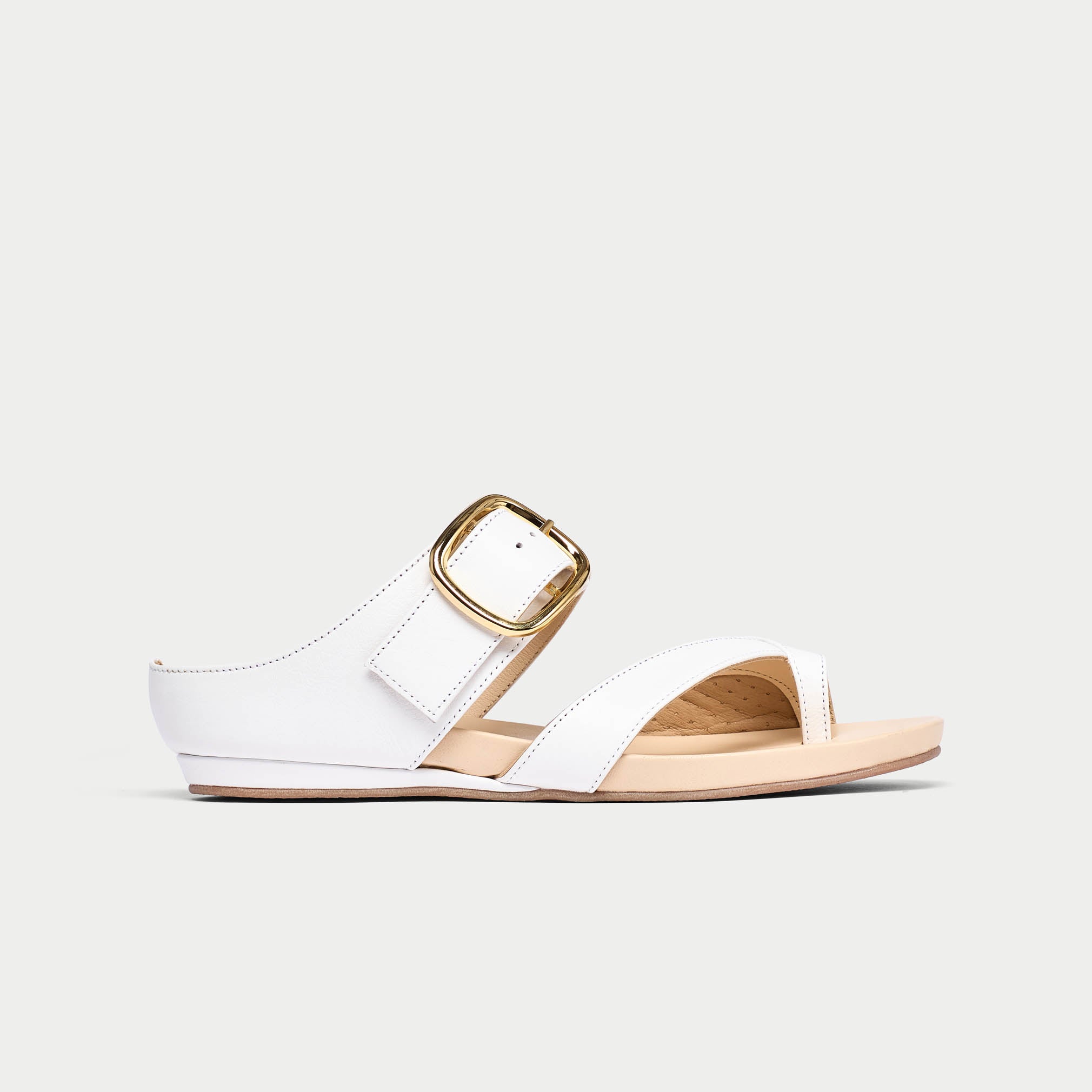 White sandal with a gold buckle on a light gray background