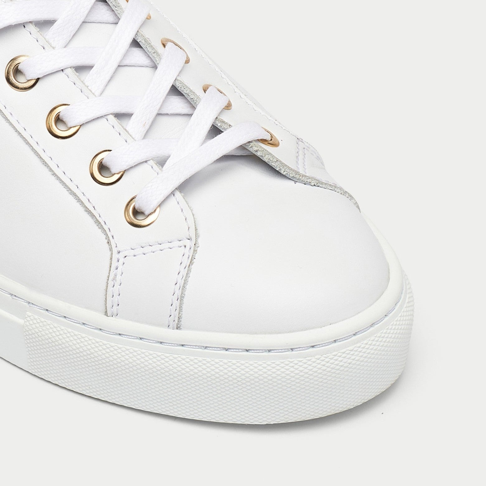 White sneaker with gold eyelets on a light gray background