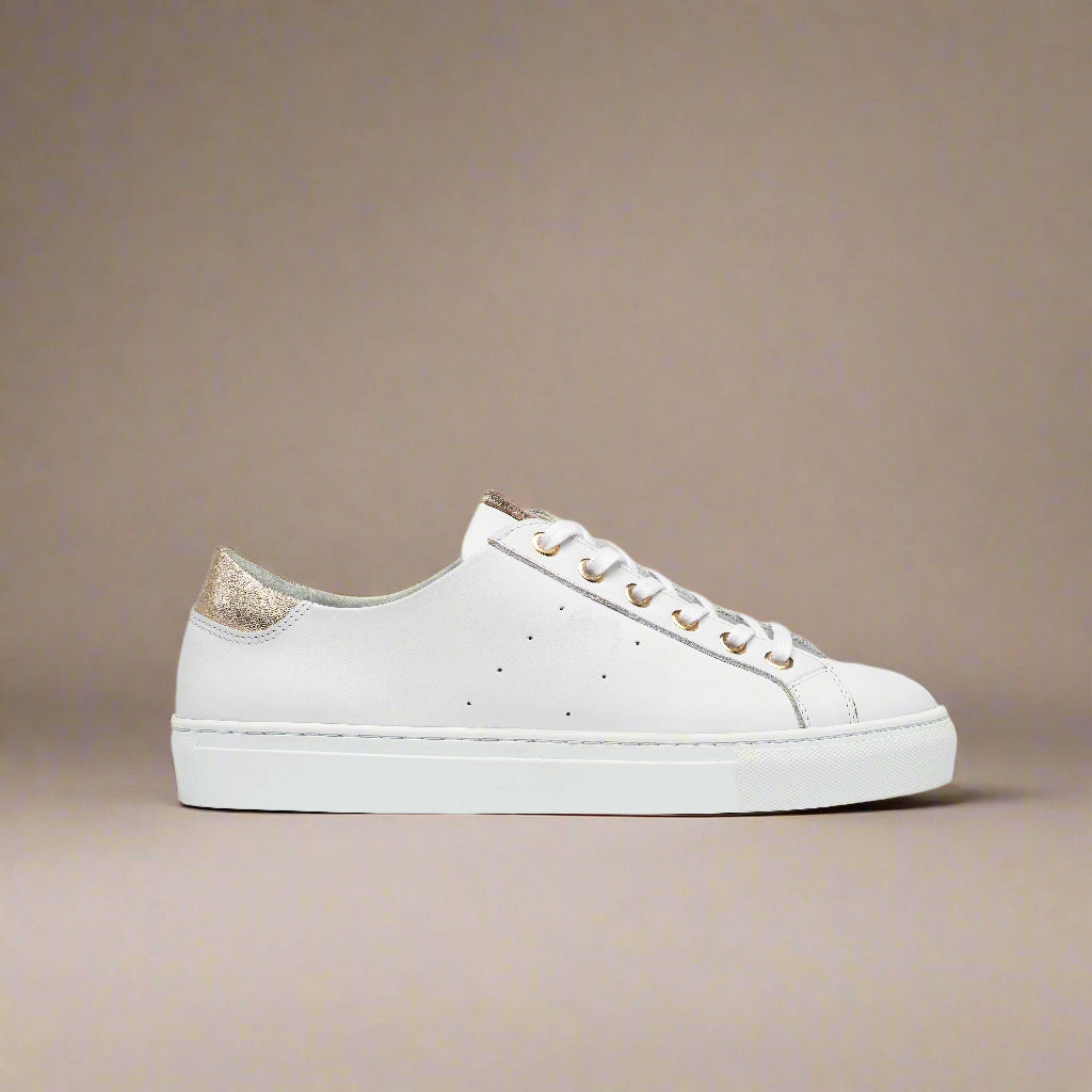 White sneaker with gold accents on a beige background