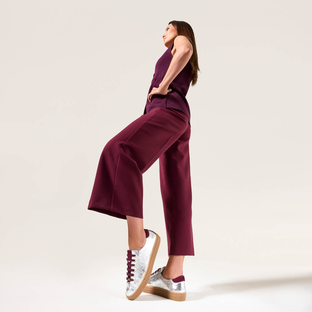 Woman wearing a purple jumpsuit with silver star sneakers on a light background