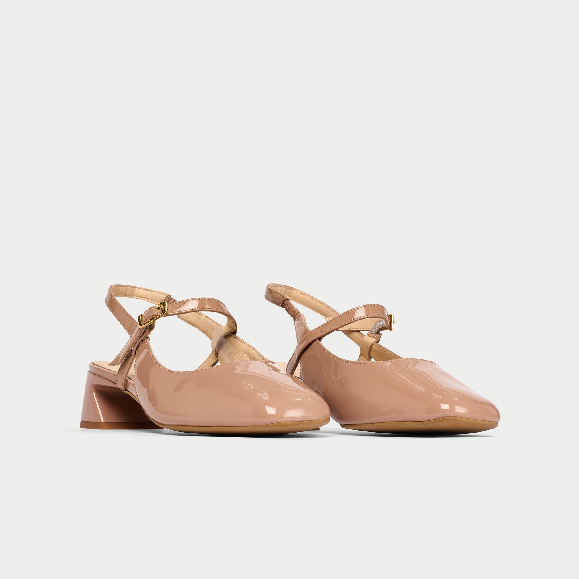 Pair of beige patent leather shoes with slingback design on a light gray background