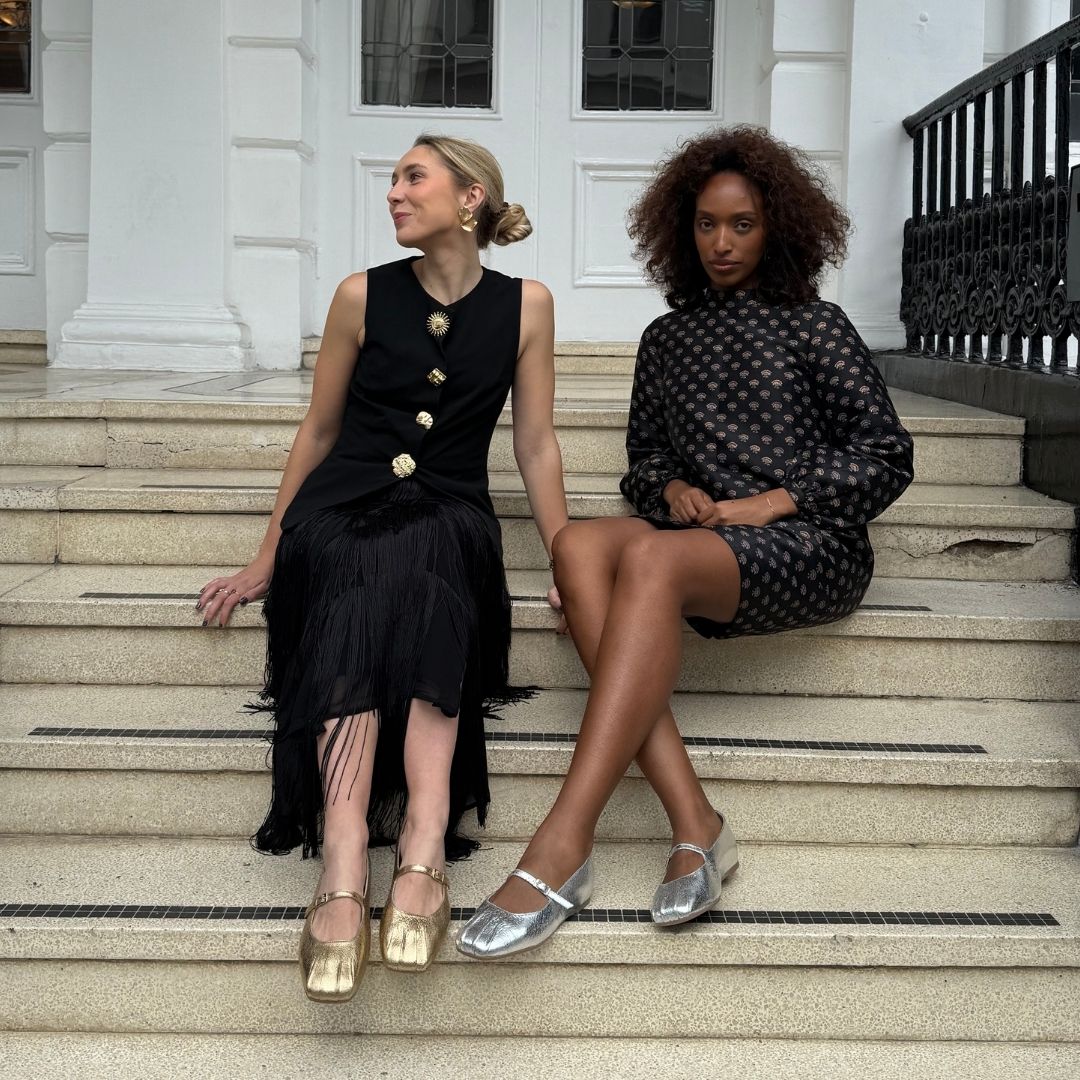 Two women sitting on steps wearing stylish outfits with gold and silver shoes.