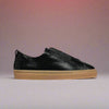 Black Estella slip-on sneaker with brown sole on a light red background