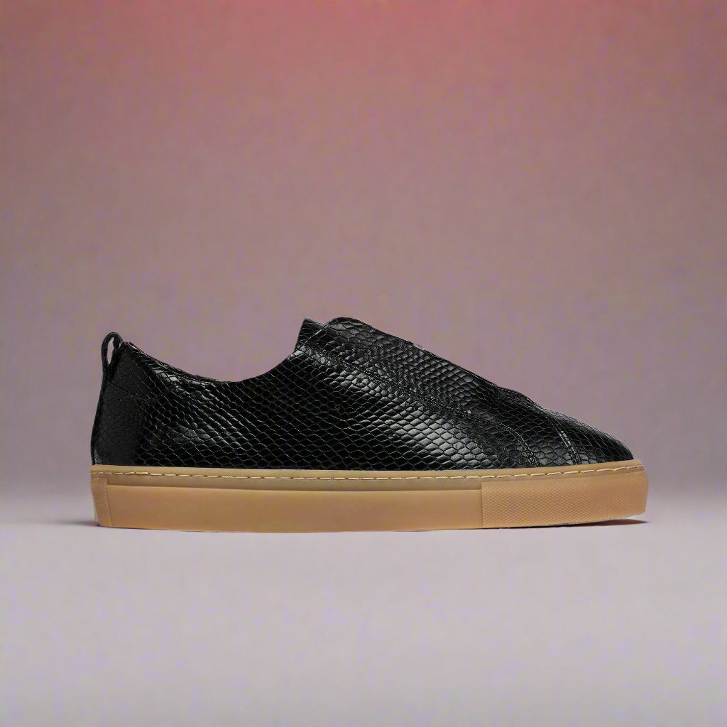 Black Estella slip-on sneaker with brown sole on a light red background