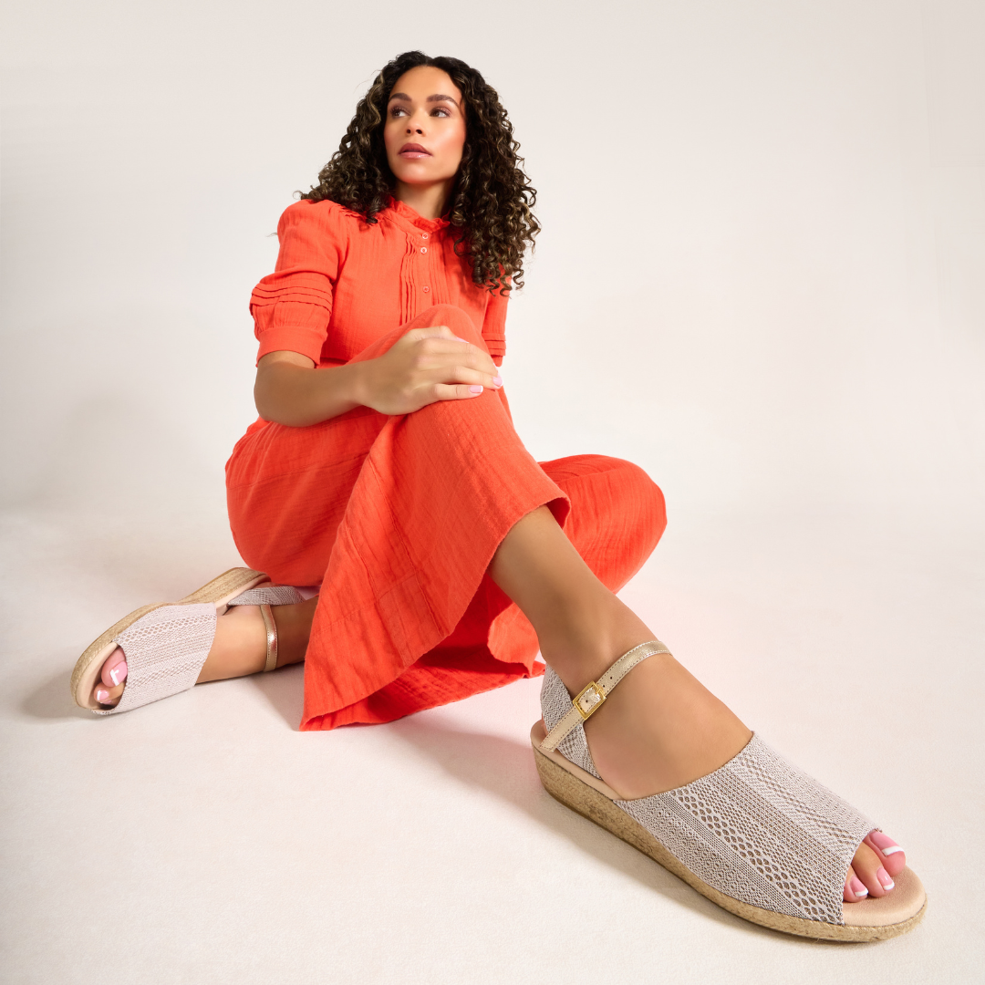 Woman wearing a bright orange dress and white sandals on a plain background