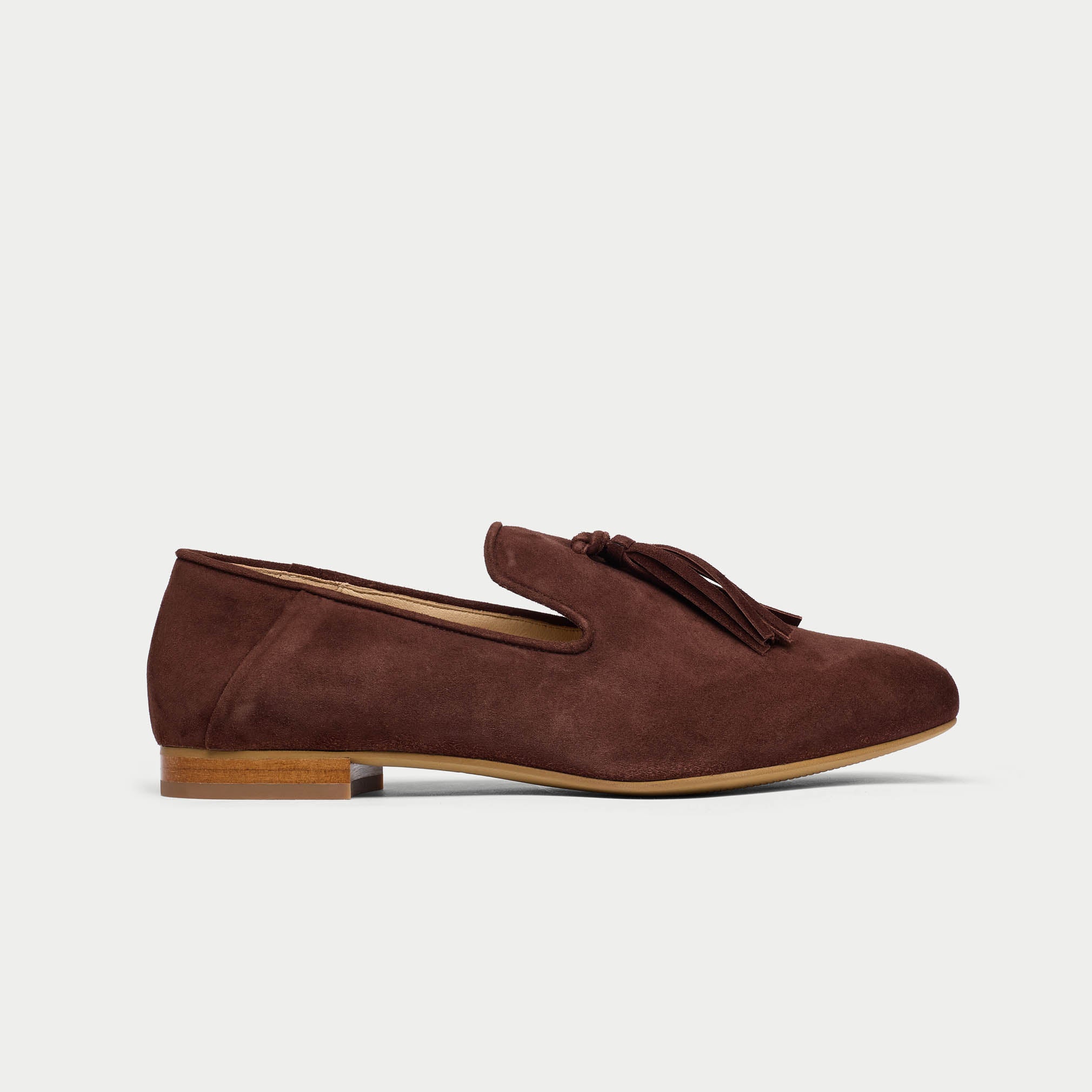 Brown suede loafer with tassel on a light gray background
