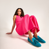 Woman wearing a bright pink dress and blue loafers sitting on a white background