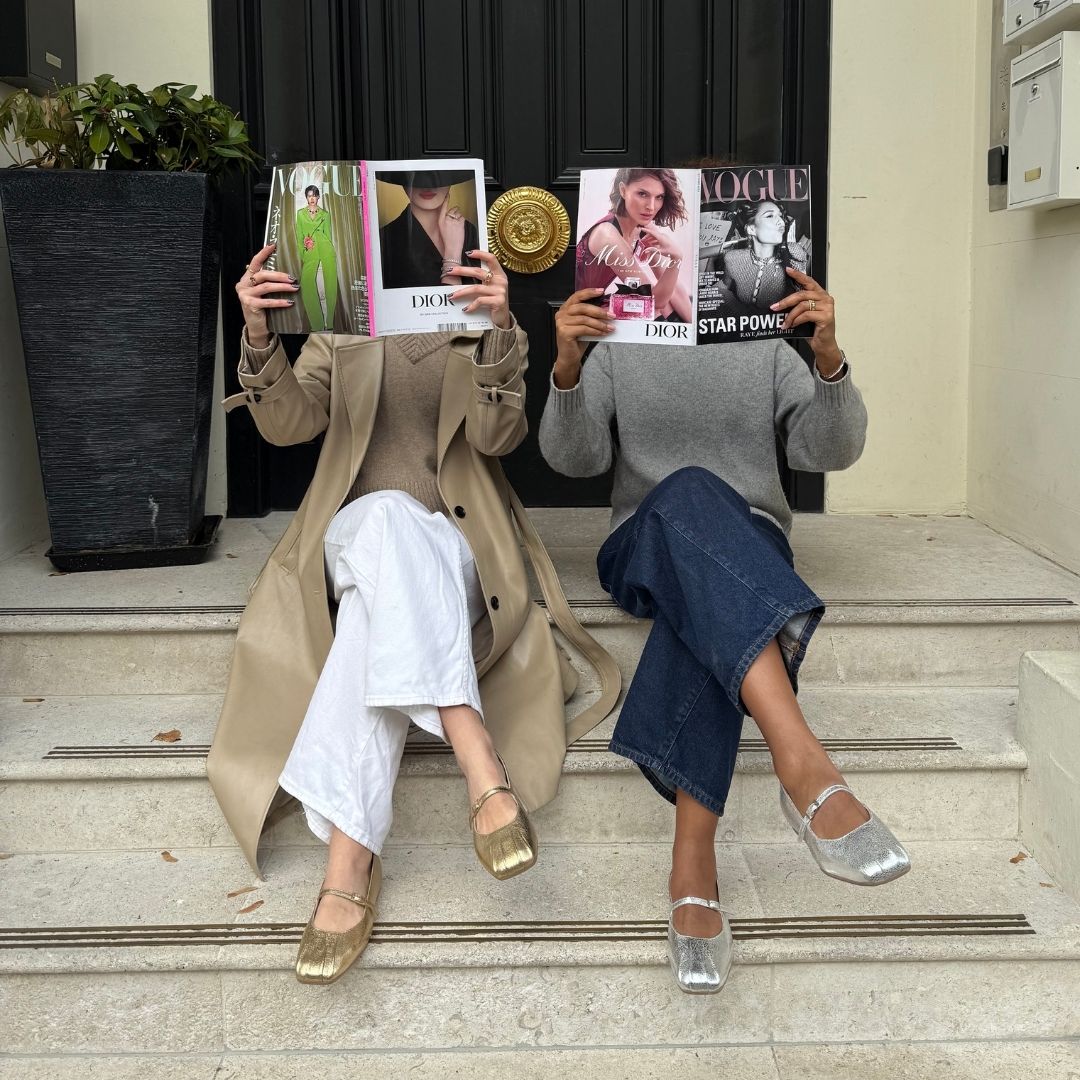 Two people sitting on steps holding up fashion magazines.