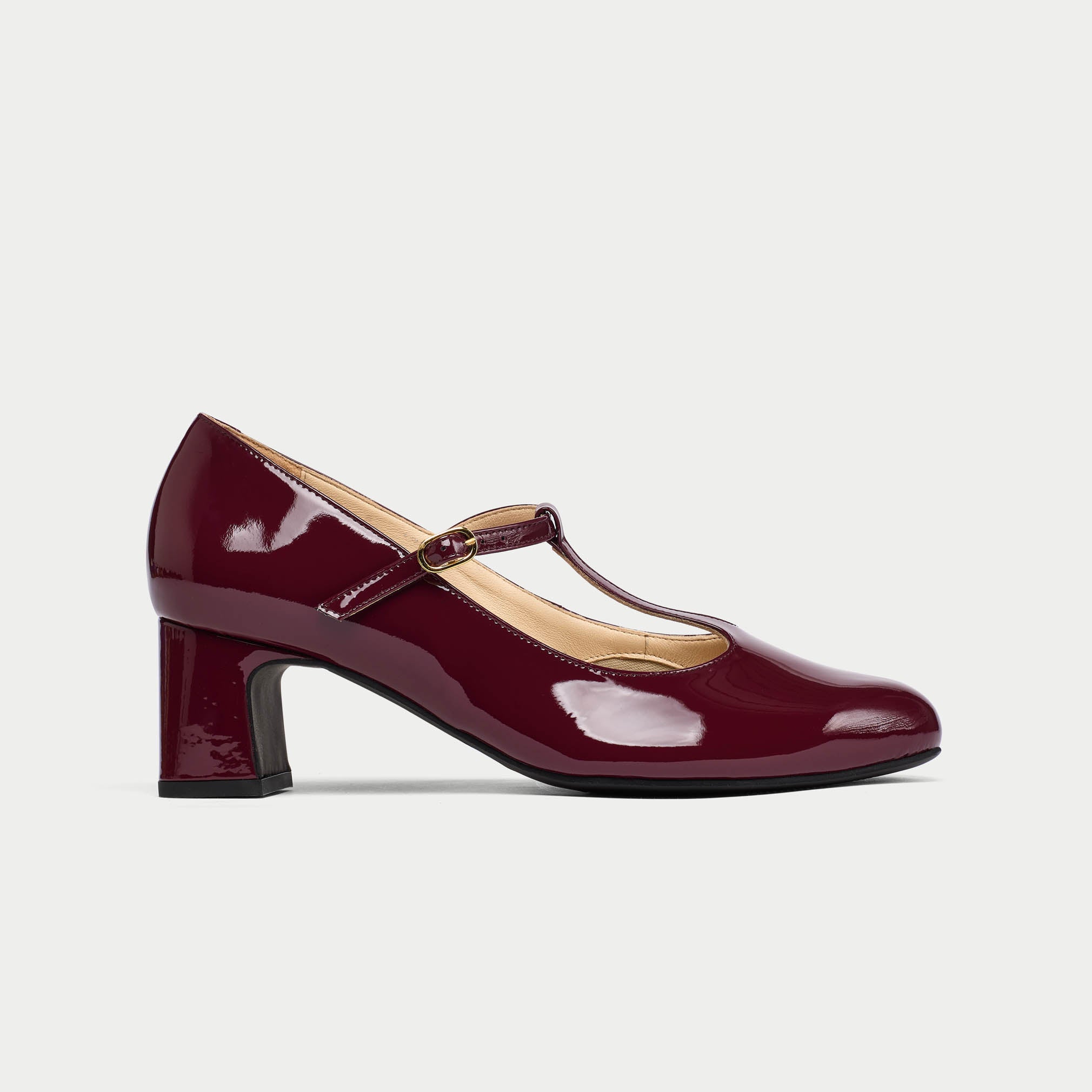 Maroon patent leather shoe with a strap on a light gray background