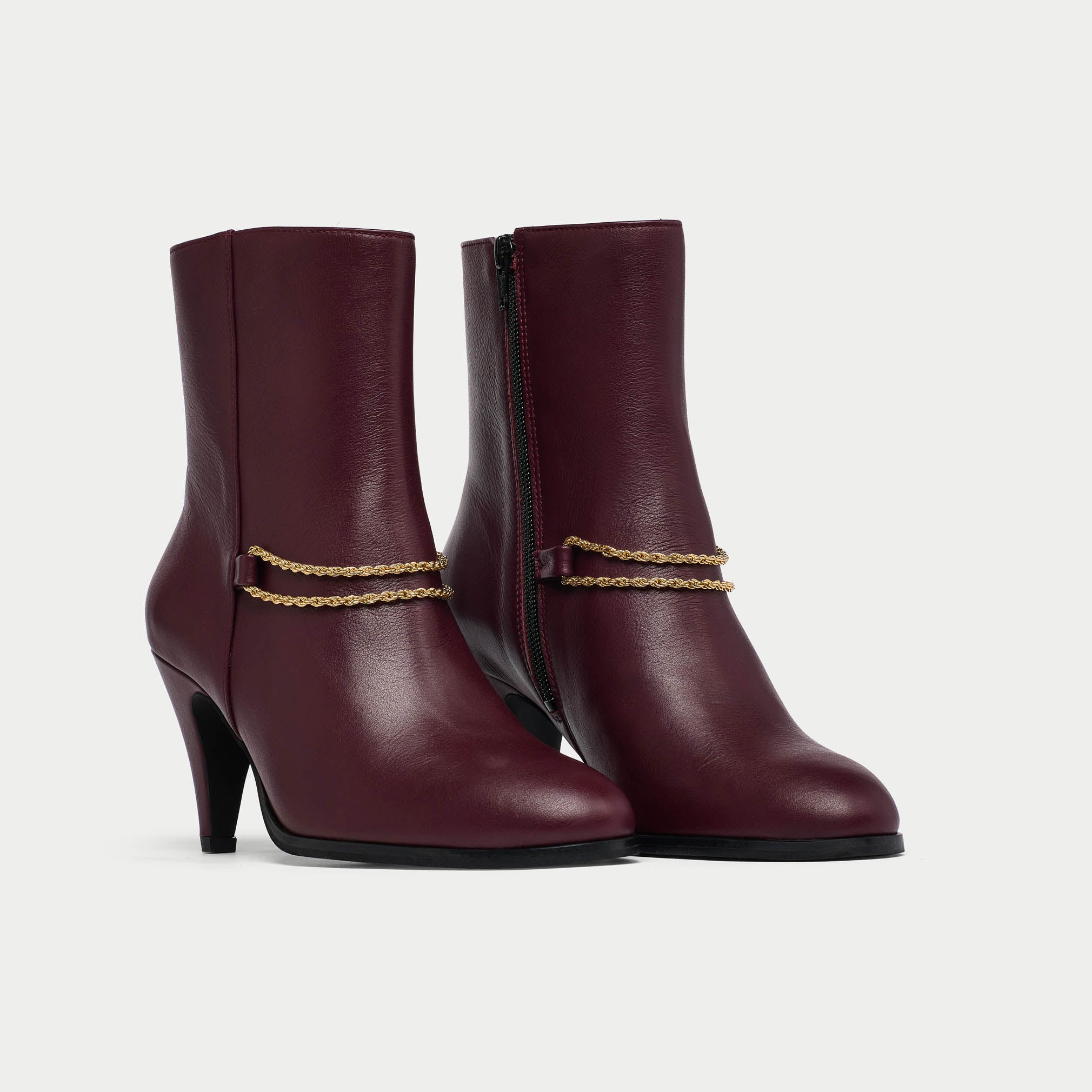 Pair of cherry Maya ankle boots with gold accents on a light gray background