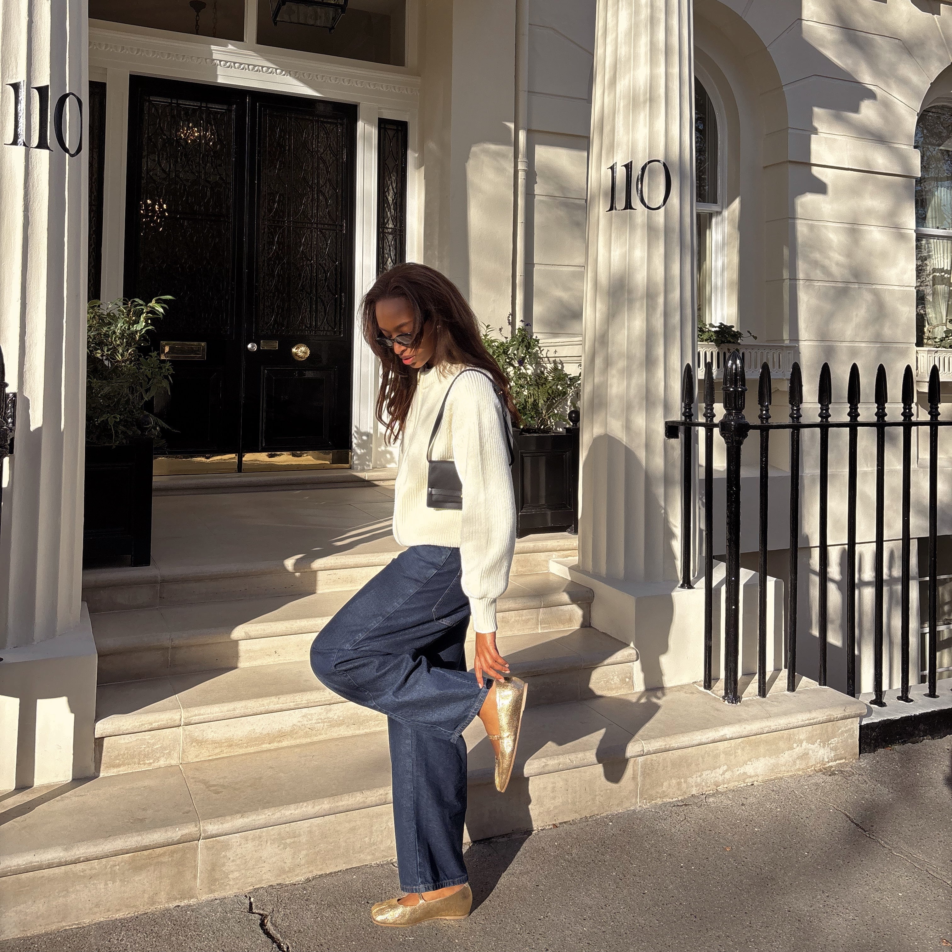 Woman posing on a set of steps in front of a large white house with columns and a black door.