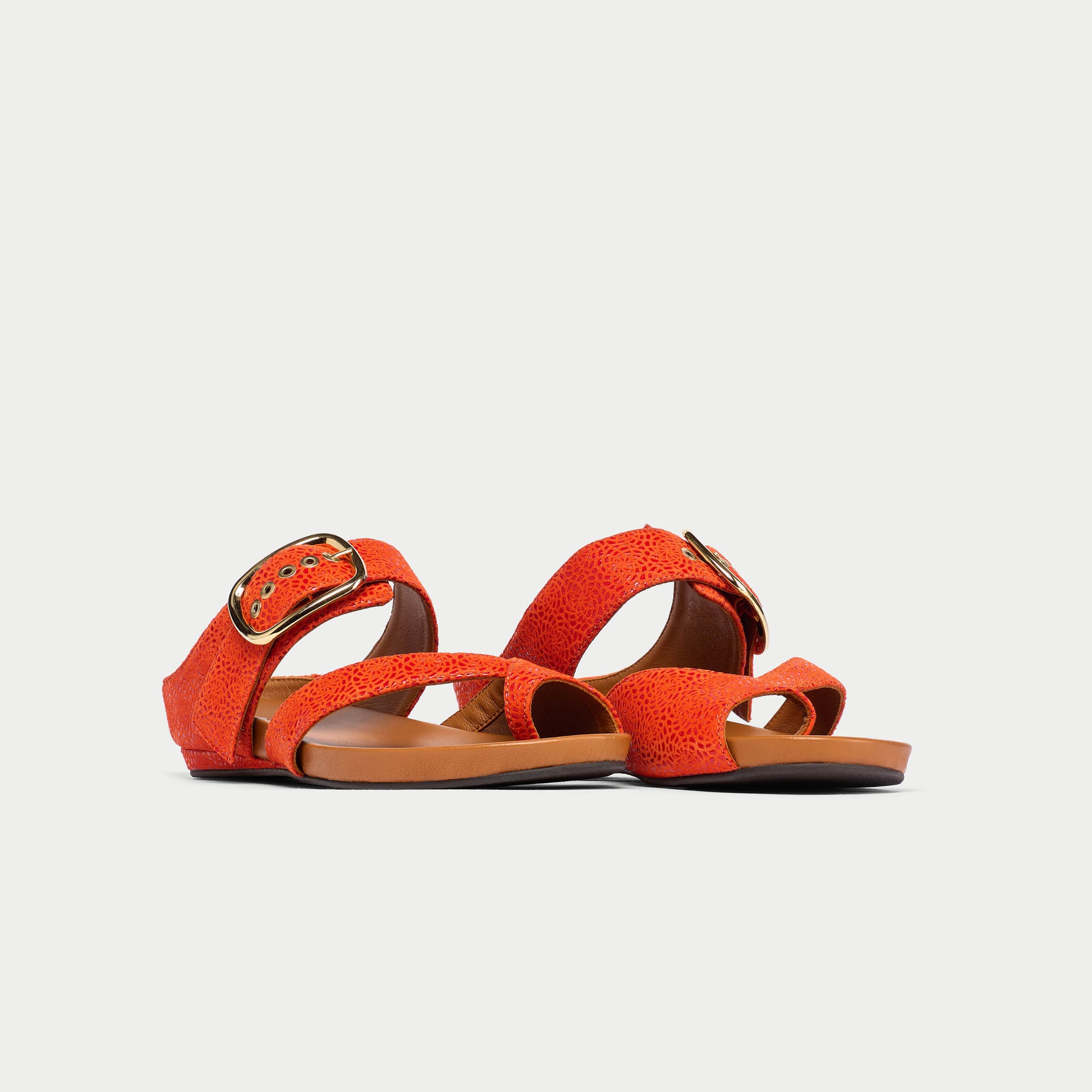 Pair of orange sandals with brown soles on a light gray background